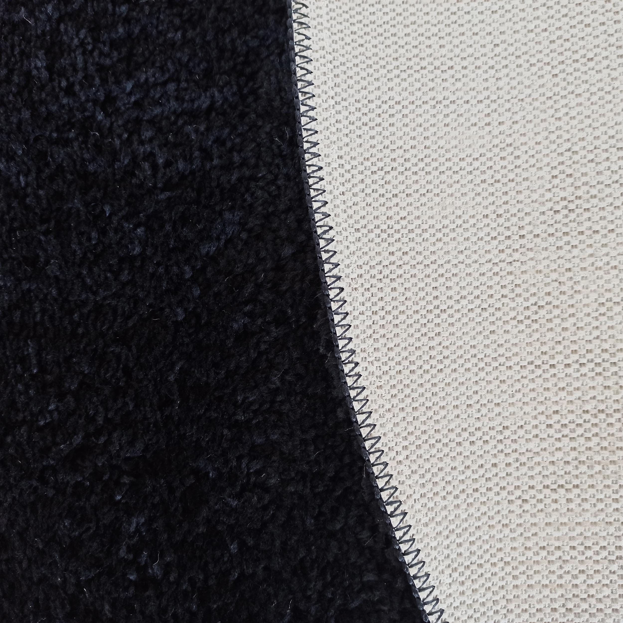 Détail d'un tapis présentant une texture à poils longs foncée et une surface tissée claire, reliées par une couture zigzag foncée