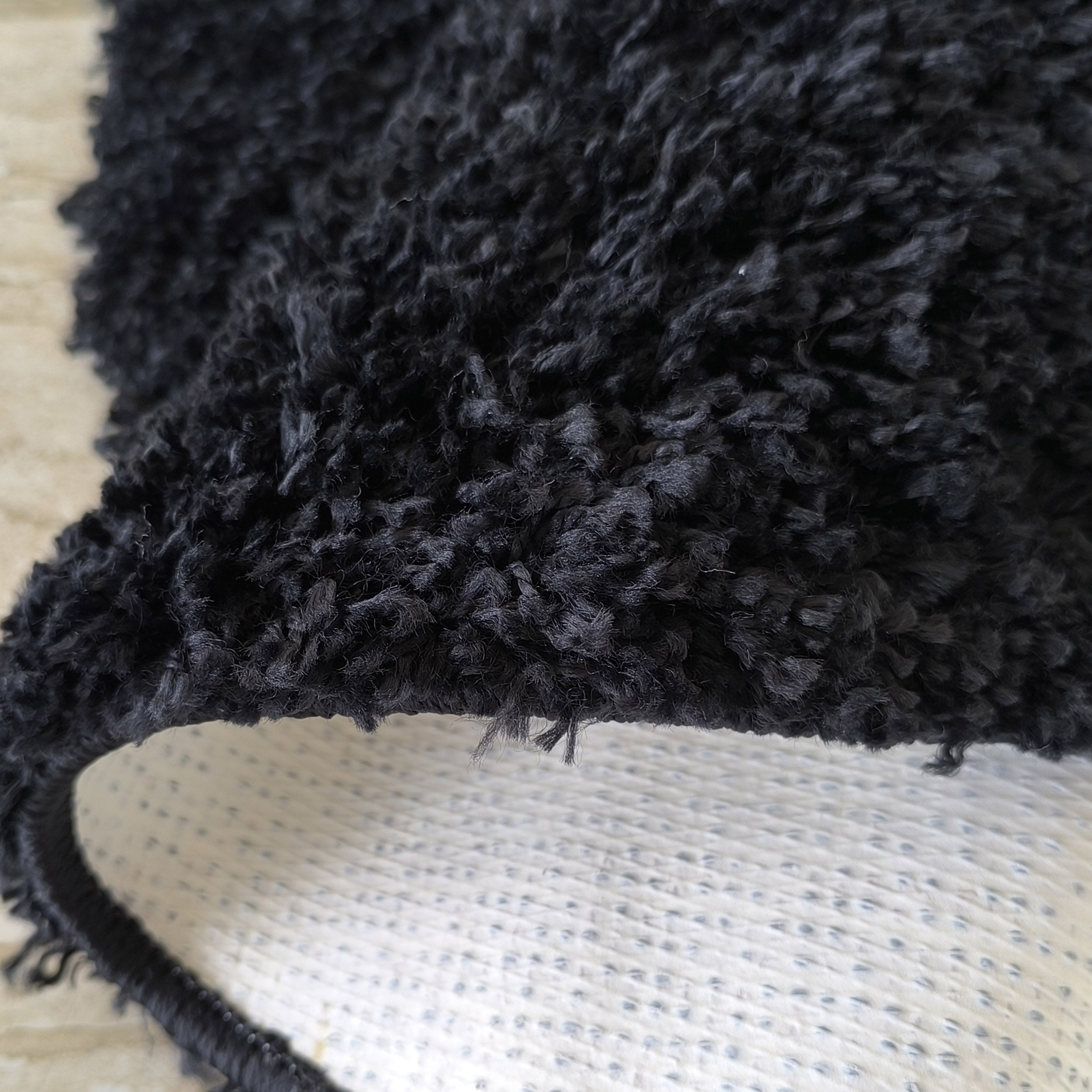 Tapis noir à poils longs et épais, dont une partie est roulée, révélant son envers blanc à motif