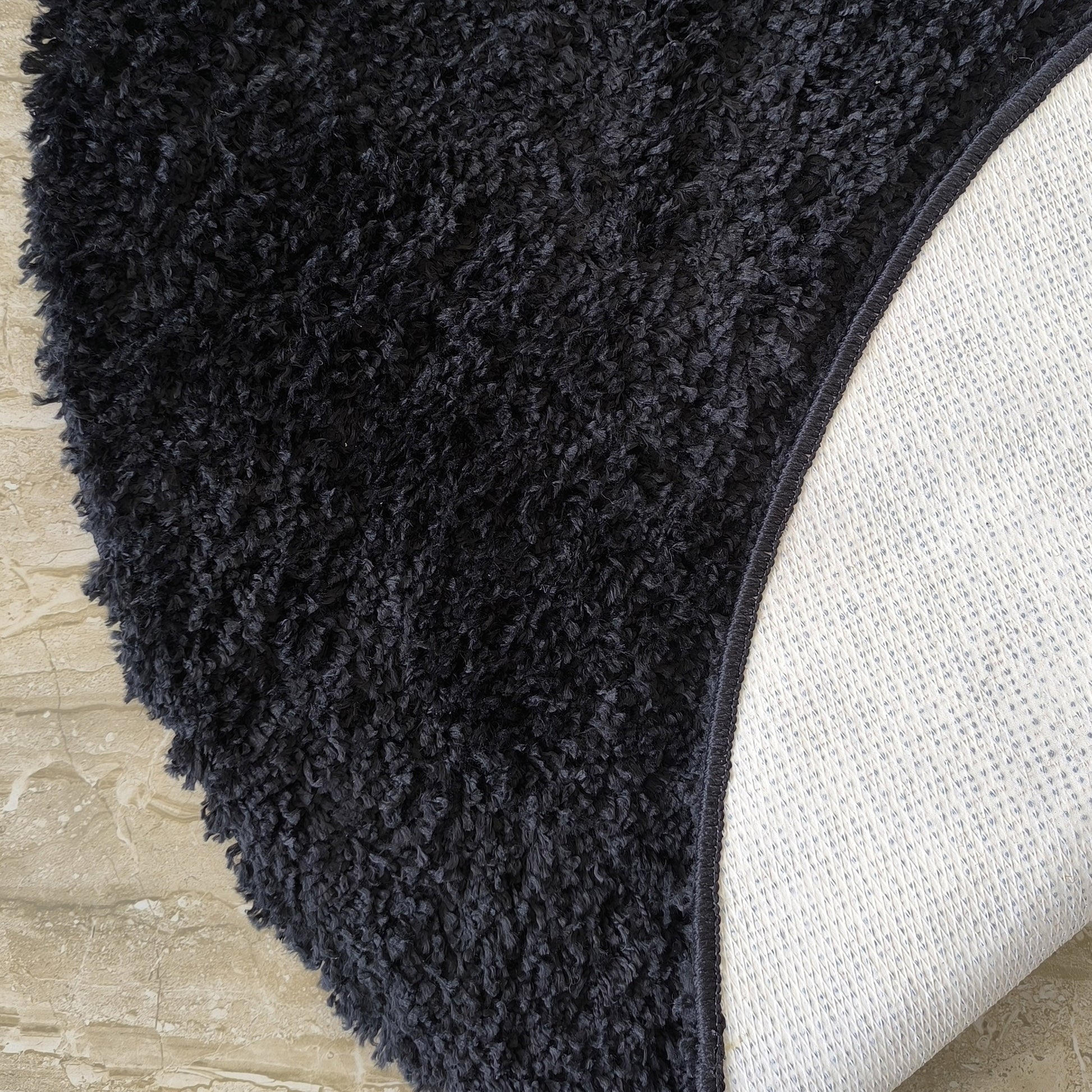 Tapis shaggy gris foncé et moelleux, partiellement enroulé sur un sol carrelé beige, révélant son envers clair antidérapant