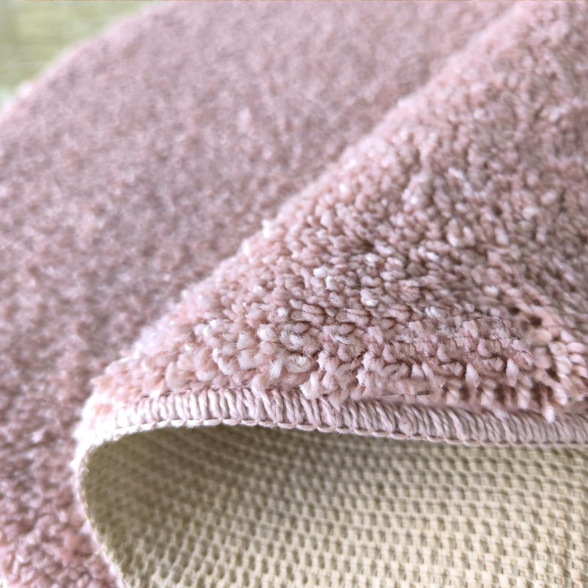 Tapis rose à poils longs et doux, dont le coin est plié, montrant son envers tissé beige
