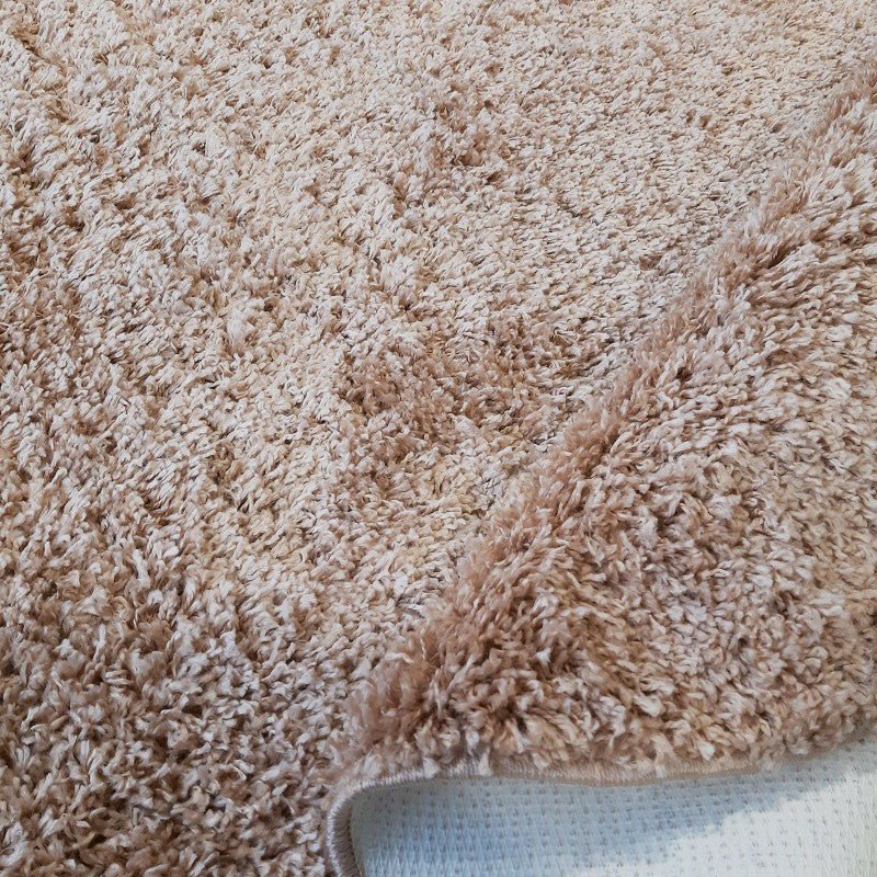 Tapis moelleux à poils longs de couleur beige clair, une partie est soulevée pour montrer son envers blanc et texturé