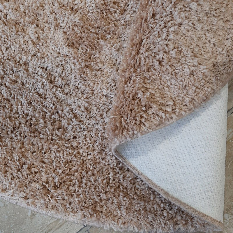 Tapis épais à poils longs de couleur beige moucheté, avec son revers blanc antidérapant visible sur un carrelage clair