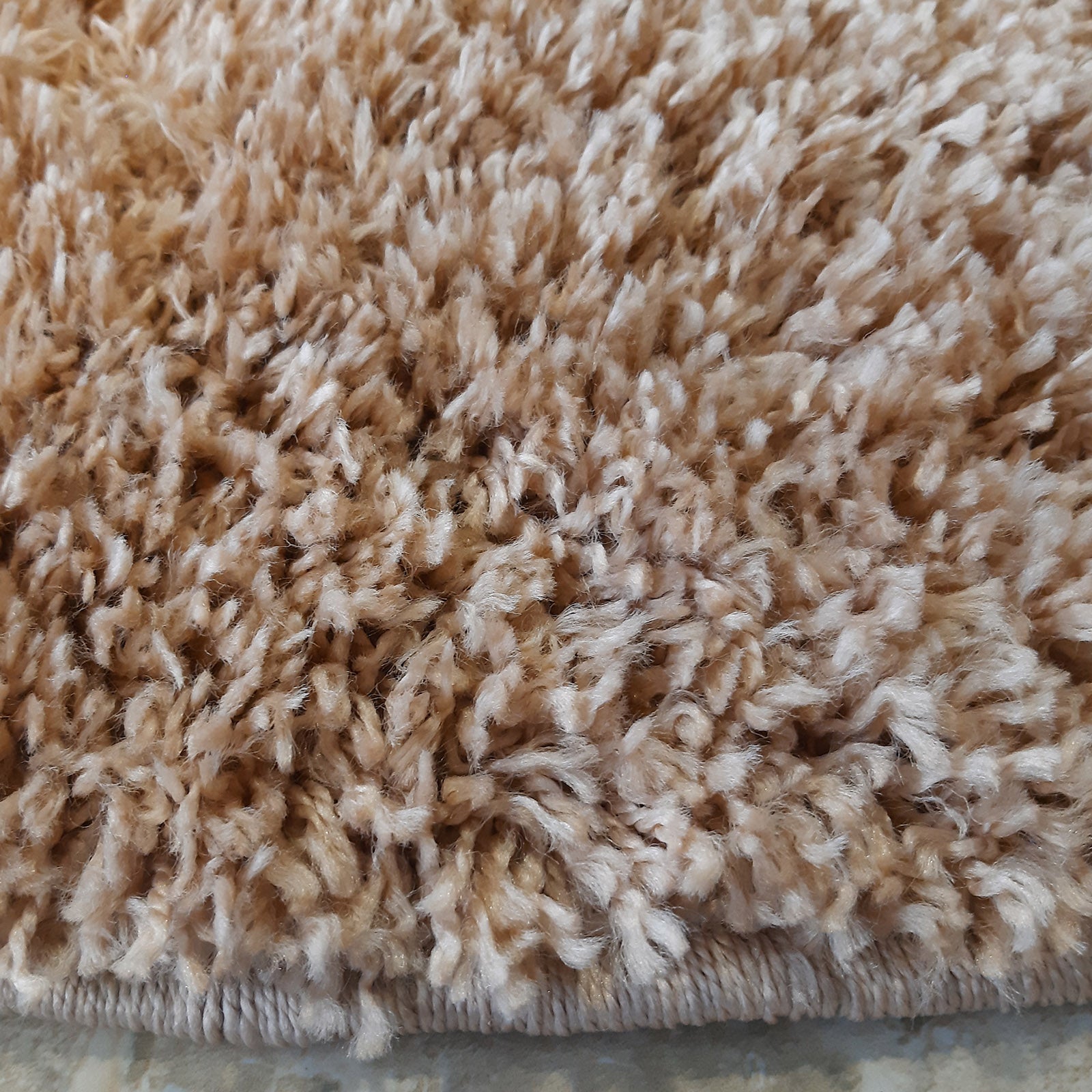 Gros plan d'un tapis beige clair à poils longs et texture moelleuse, avec une bordure tressée visible