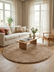 Tapis rond shaggy beige à poils longs, posé sur un parquet en bois clair dans un salon lumineux