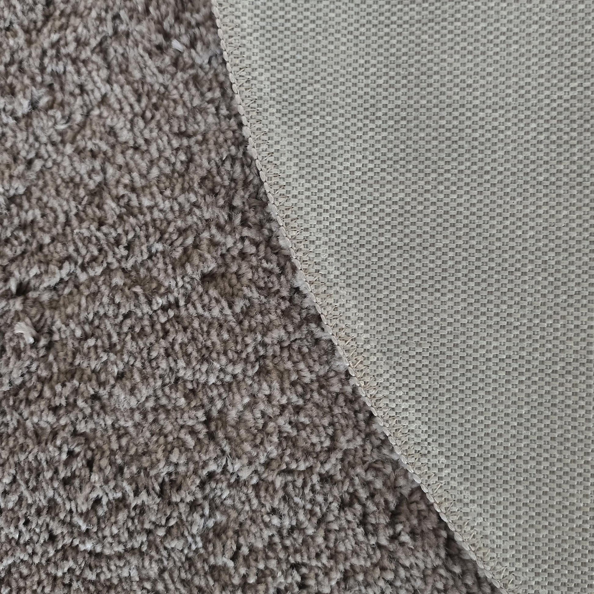Gros plan sur un tapis montrant sa surface douce à poils longs gris-brun et son envers tissé à motif quadrillé beige