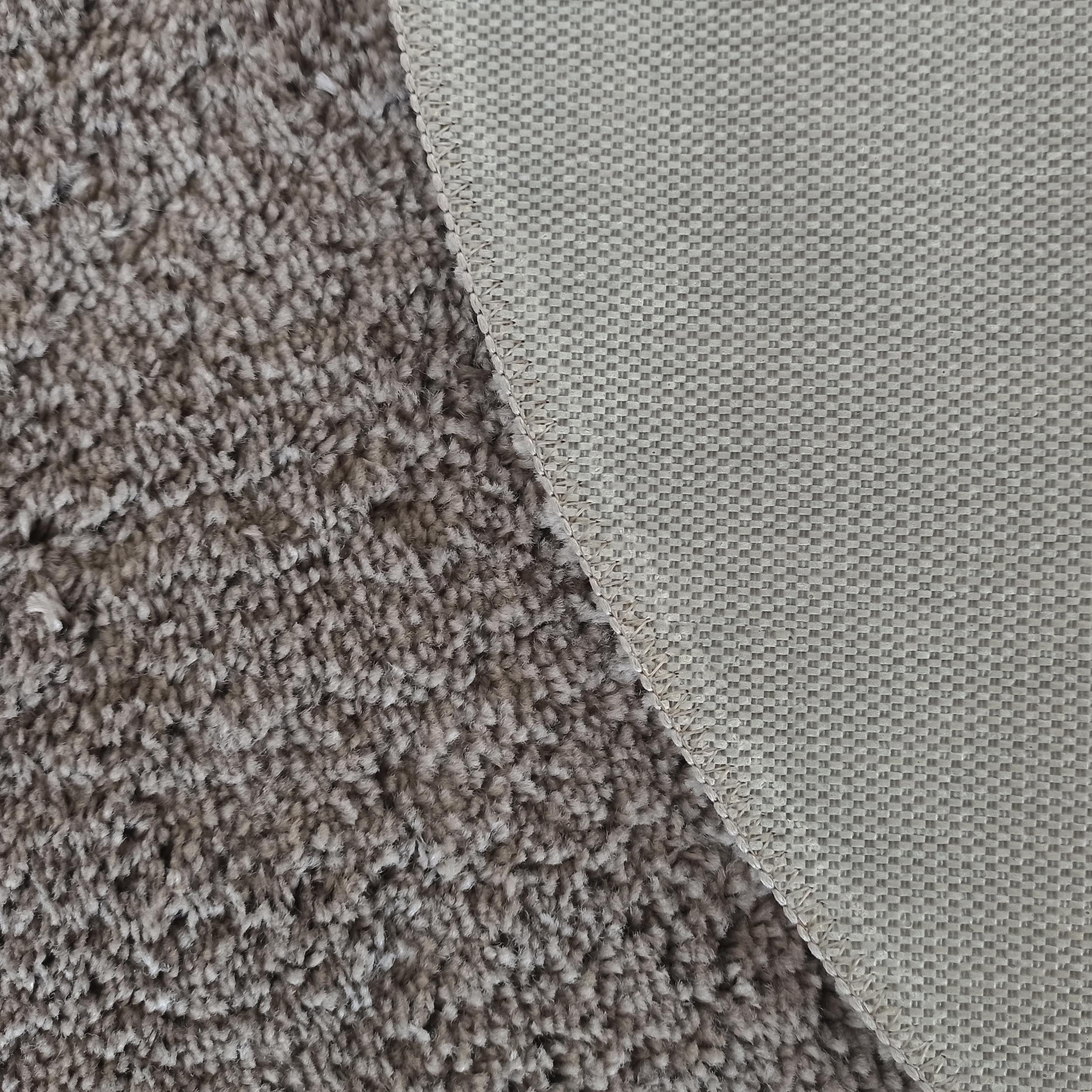 Gros plan sur un tapis montrant sa surface douce à poils longs gris-brun et son envers tissé à motif quadrillé beige