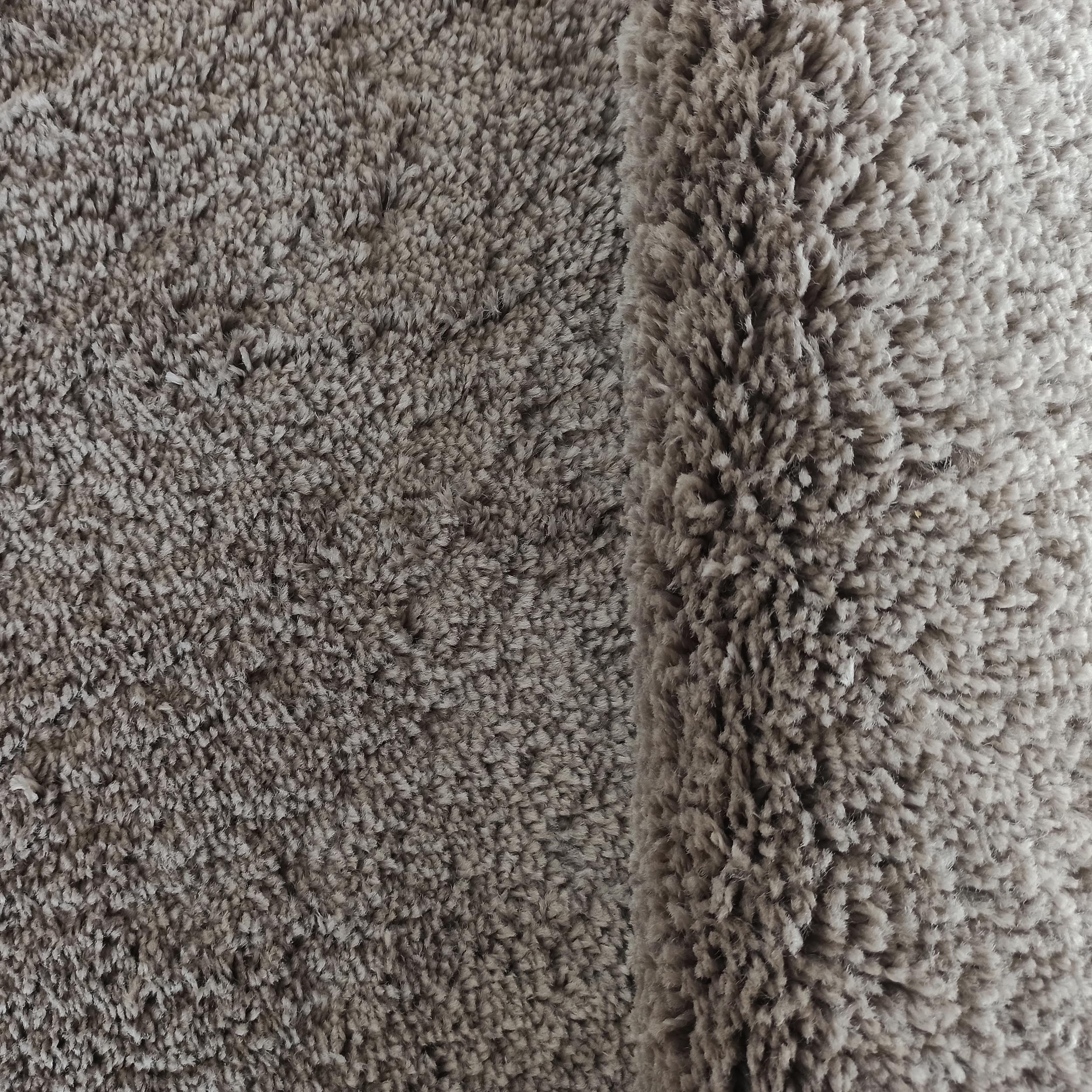 Tapis moelleux à poils longs de couleur taupe, présentant une texture douce et un pli sur le côté droit