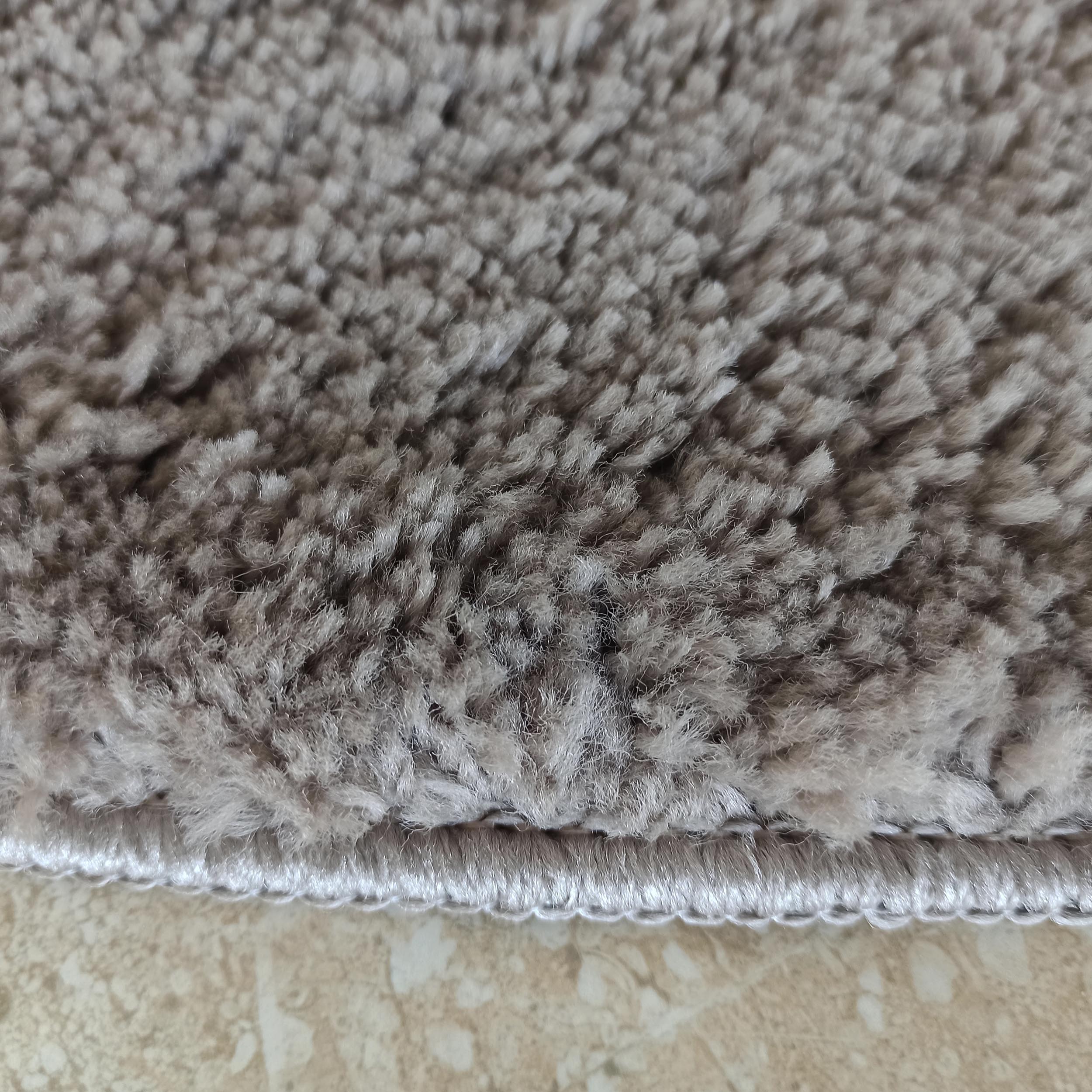 Tapis gris clair à poils longs et doux, avec une bordure blanche côtelée au-dessus d'un sol carrelé beige