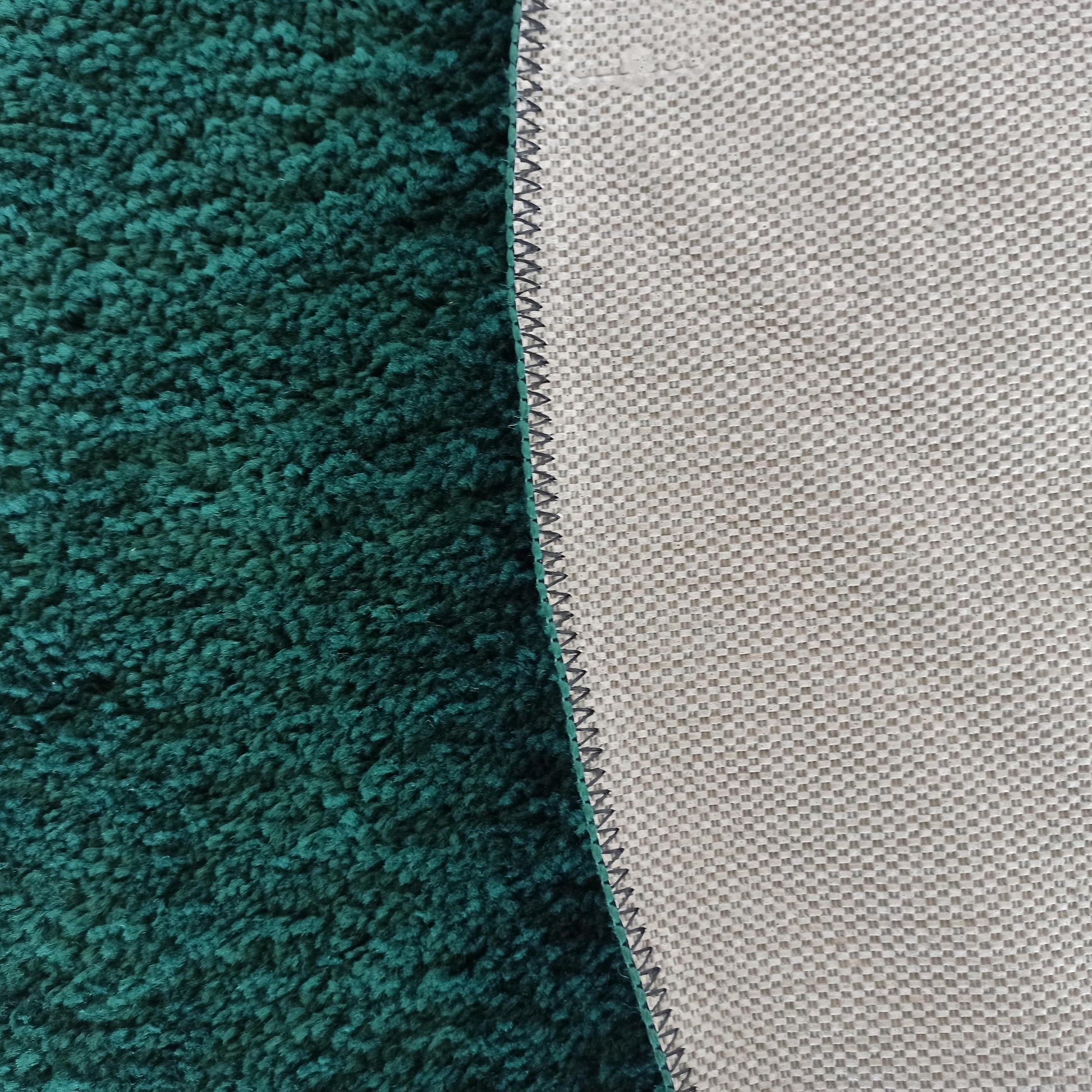 Un tapis vert foncé à poils longs visible avec son envers gris clair texturé en quadrillage