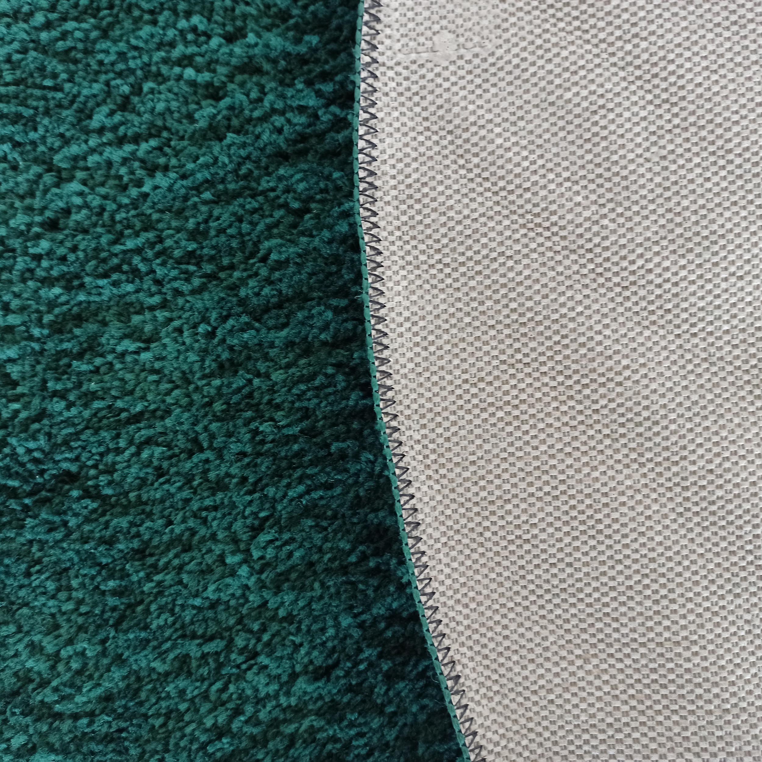 Un tapis vert foncé à poils longs visible avec son envers gris clair texturé en quadrillage