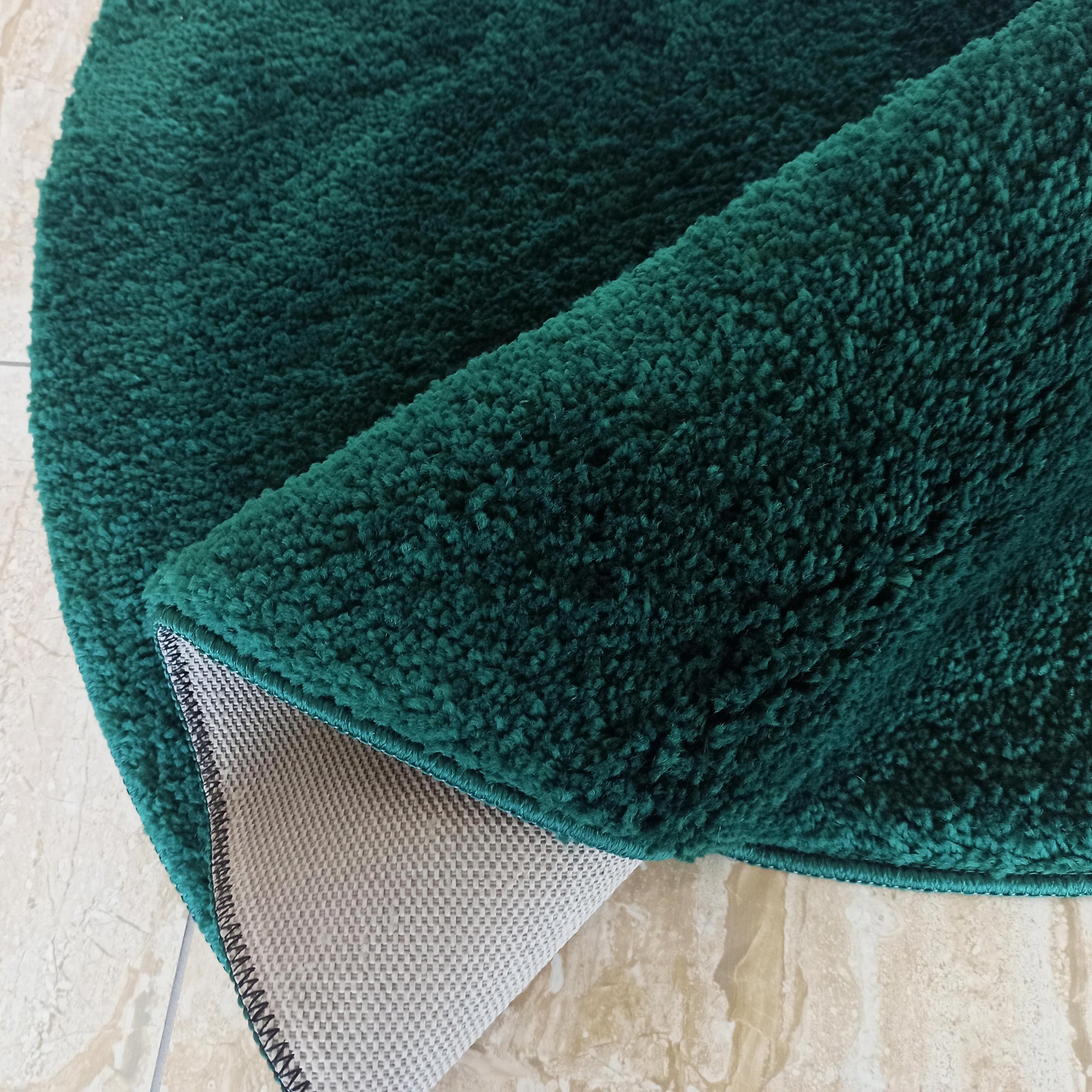 Tapis vert émeraude à poils longs, partiellement roulé, dévoilant son envers antidérapant gris clair sur un carrelage