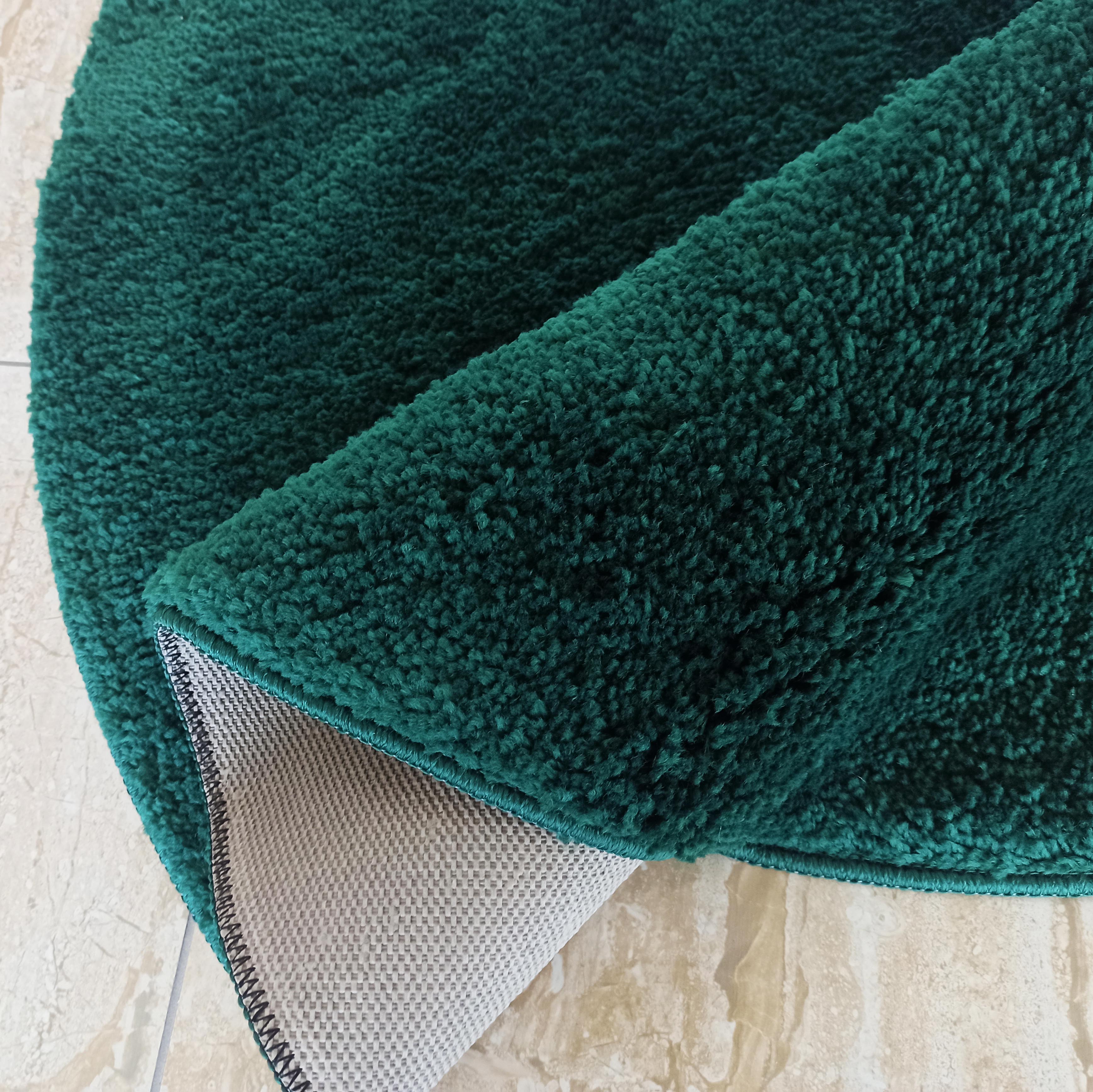 Tapis vert émeraude à poils longs, partiellement roulé, dévoilant son envers antidérapant gris clair sur un carrelage
