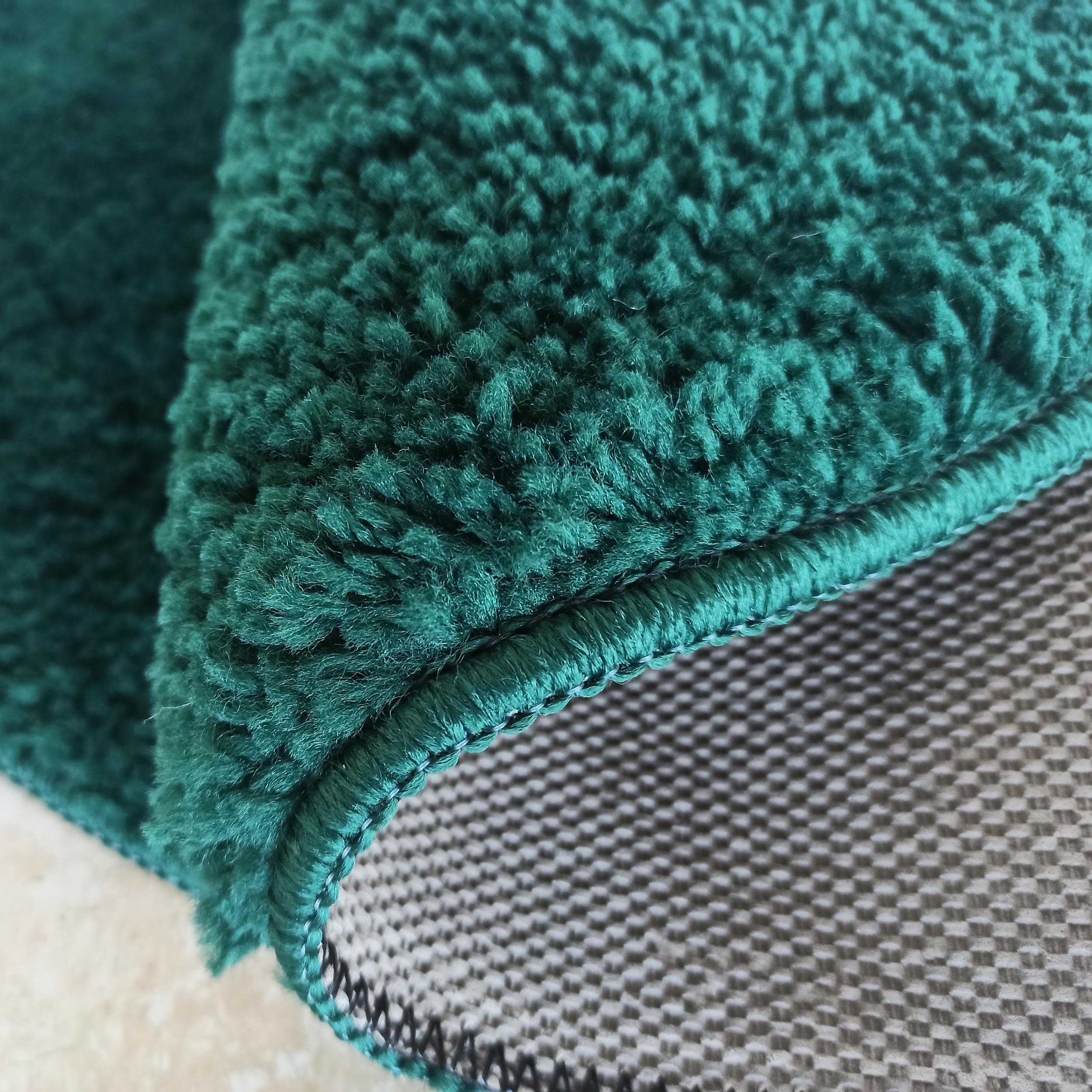 Tapis vert sarcelle moelleux à poils longs, avec bord ourlé et revers gris foncé antidérapant visible