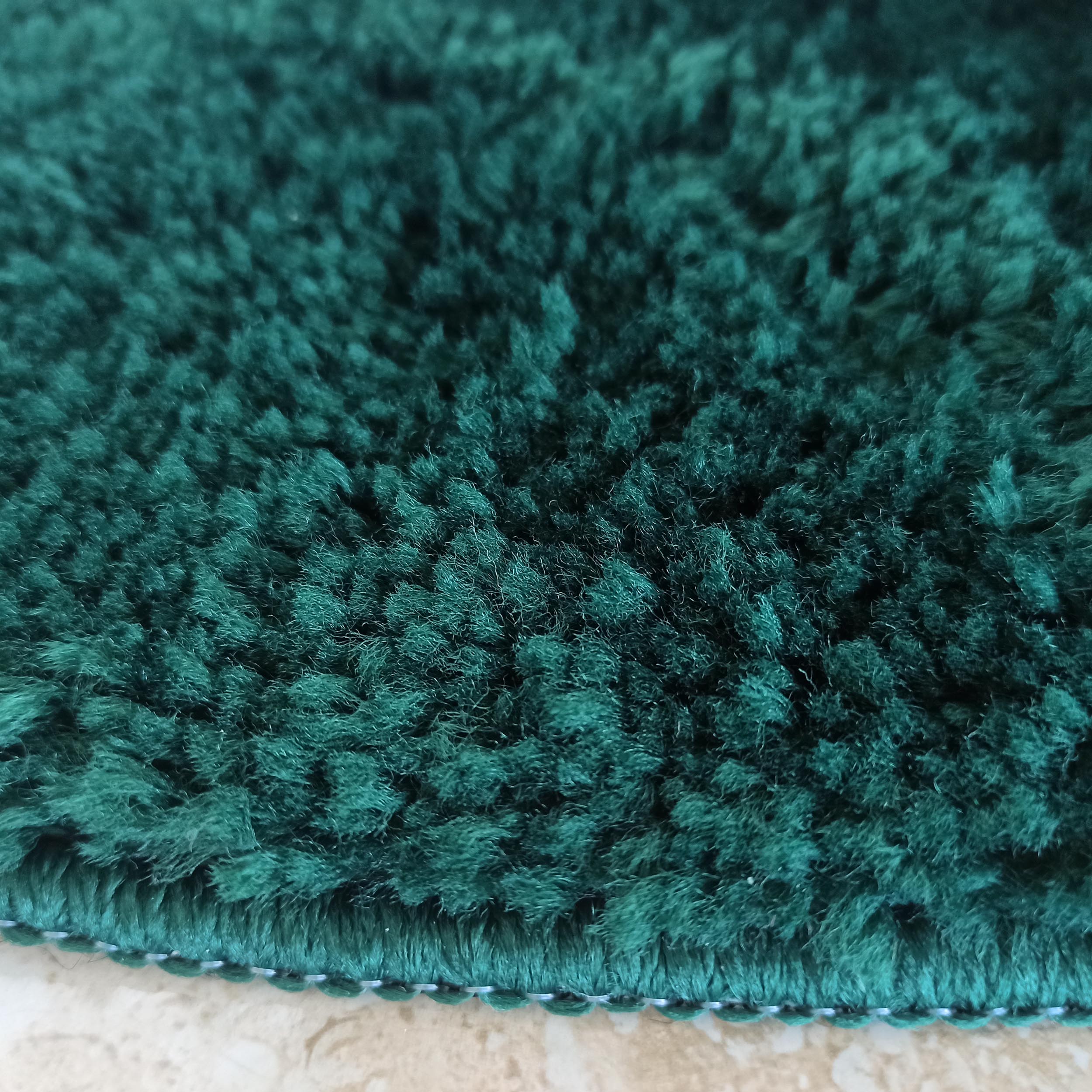 Gros plan d'un tapis vert émeraude à poils longs, avec une texture dense et un bord cousu apparent sur un sol clair