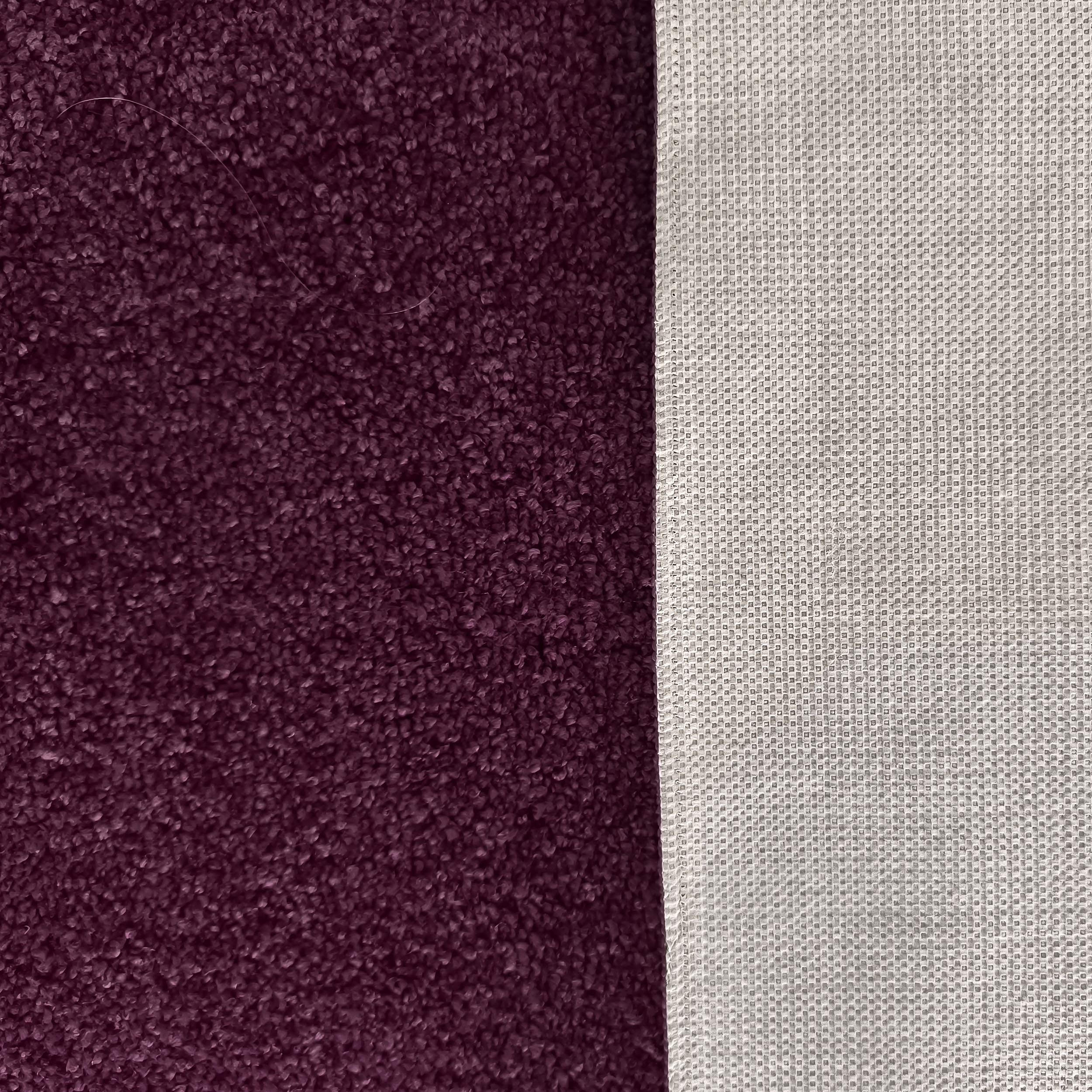 Gros plan sur un tapis violet foncé à la texture épaisse et son envers gris clair présentant un motif quadrillé
