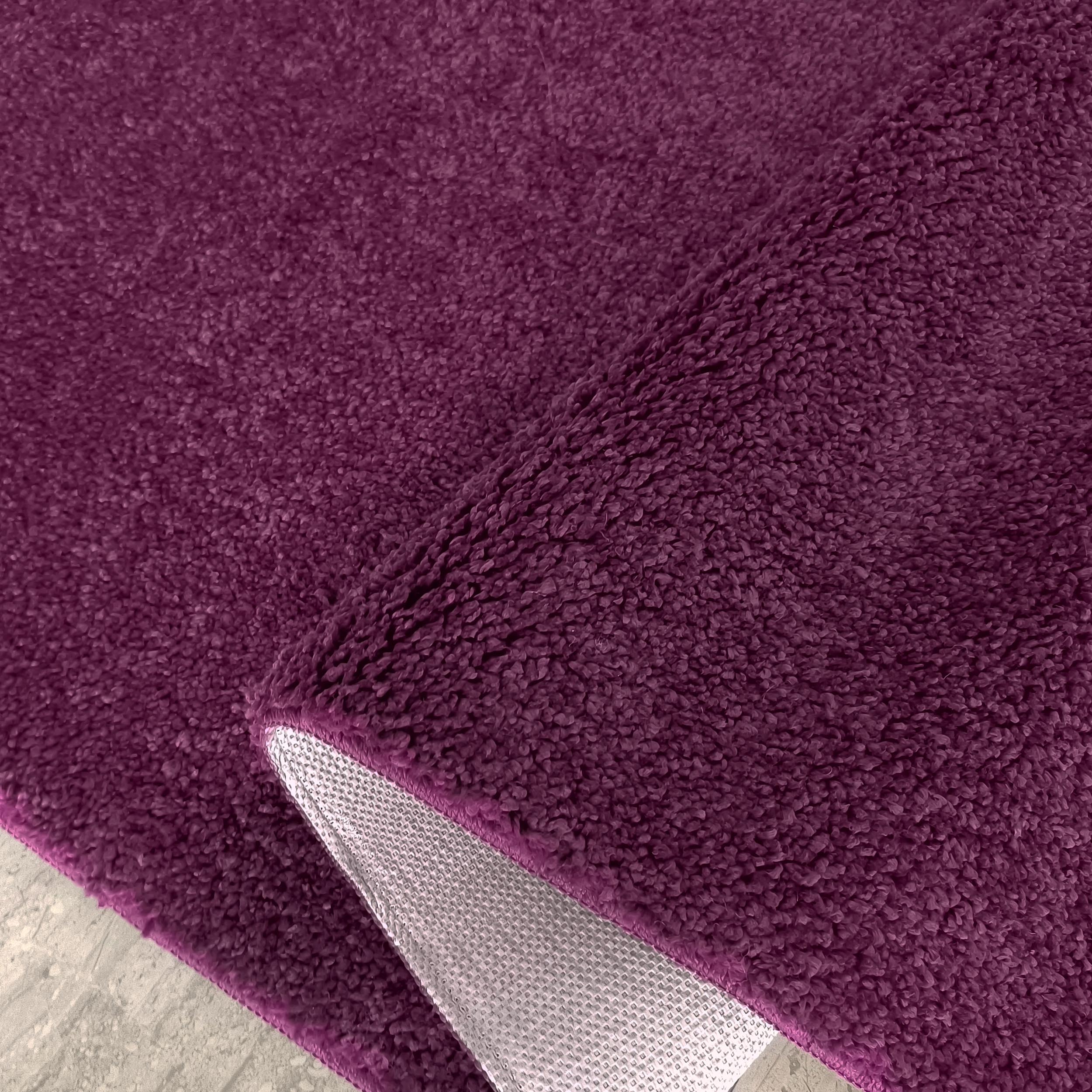Tapis doux et moelleux de couleur pourpre, avec un coin relevé montrant son envers texturé gris clair