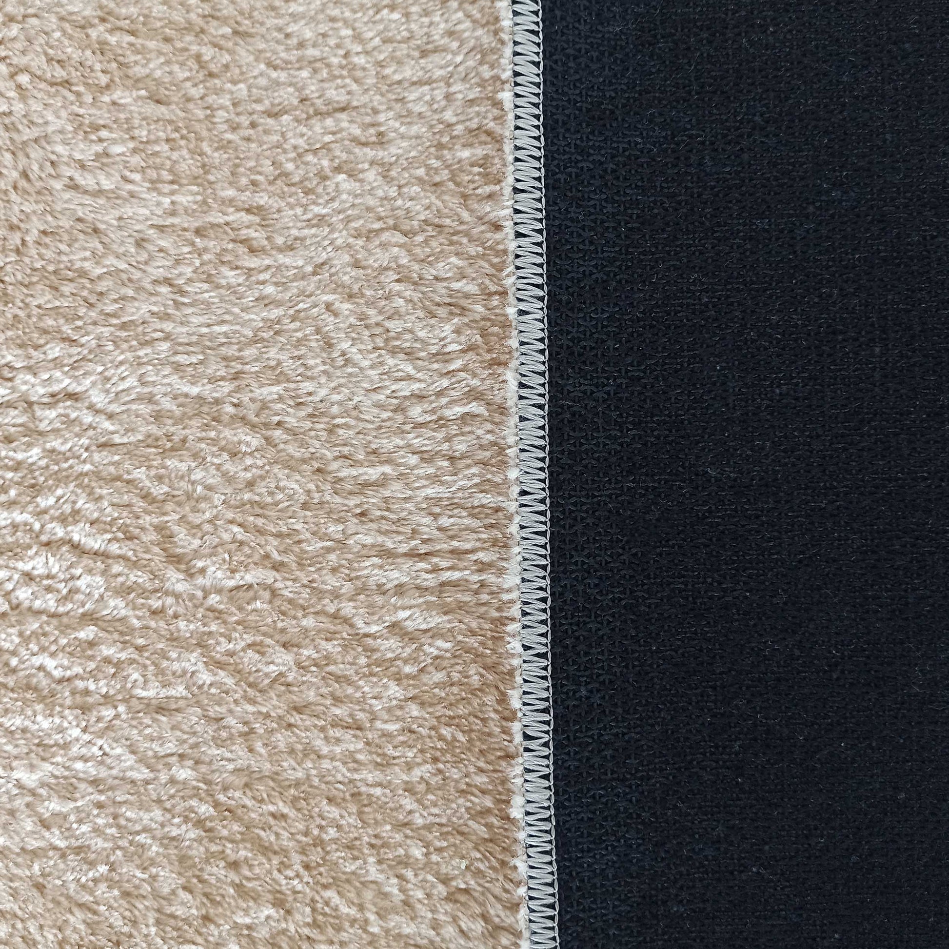 Gros plan d'un tapis bicolore, avec une surface beige à poils longs et une surface noire tissée, unies par une couture blanche