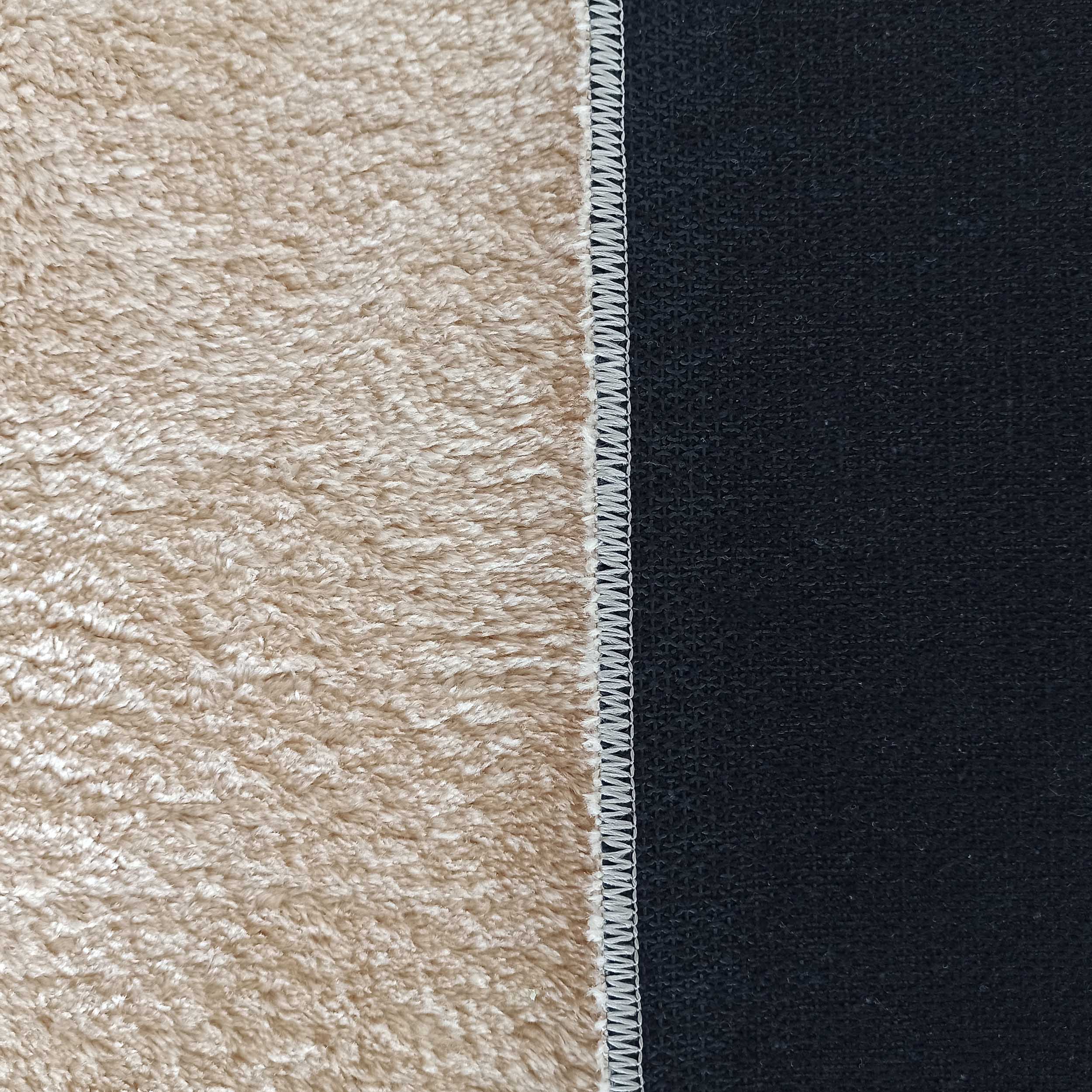 Gros plan d'un tapis bicolore, avec une surface beige à poils longs et une surface noire tissée, unies par une couture blanche