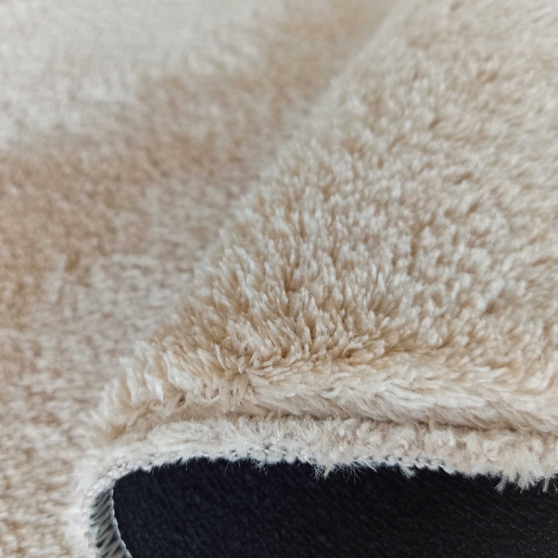 Gros plan sur la texture d'un tapis épais et duveteux de couleur beige crème, avec un côté sombre visible