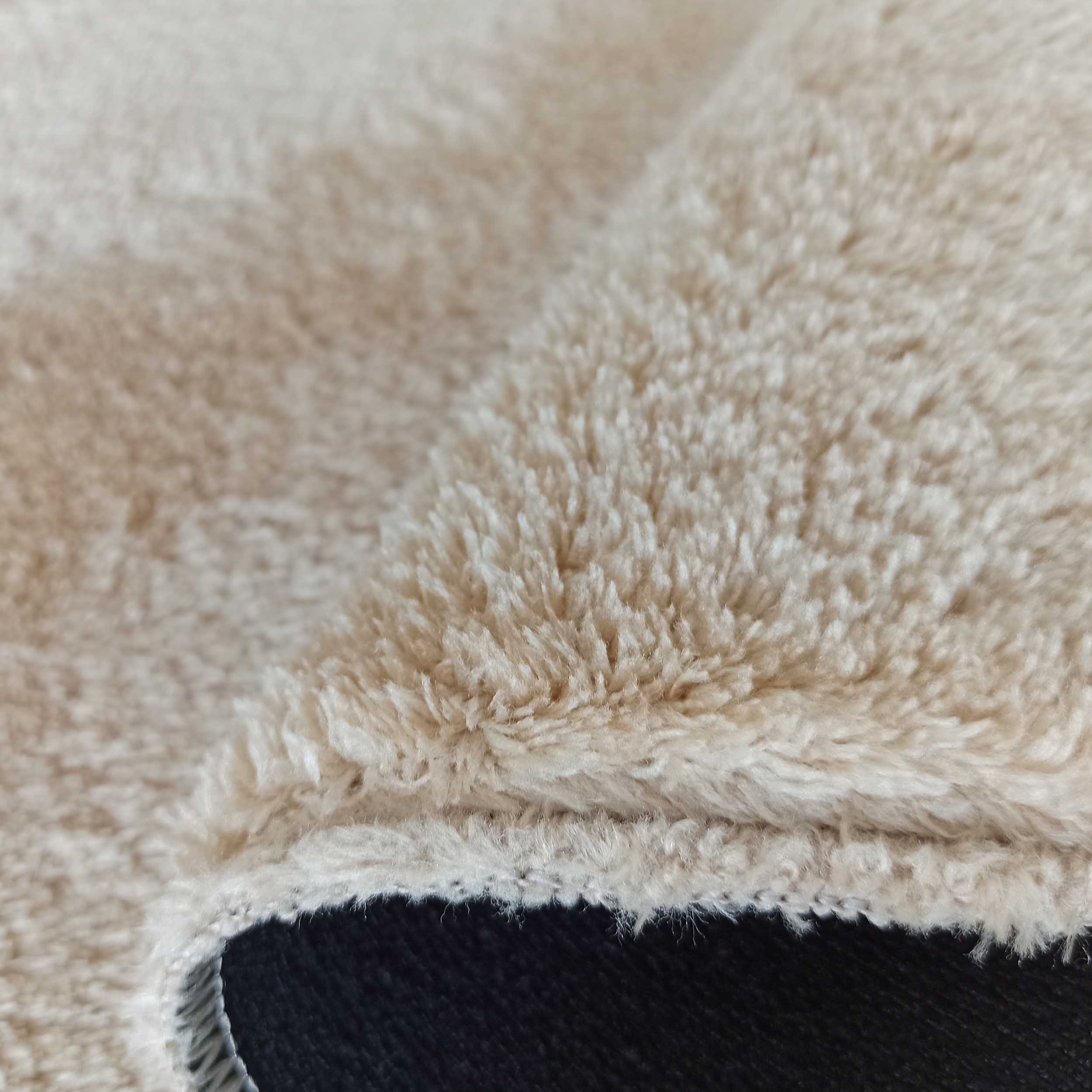 Gros plan sur la texture d'un tapis épais et duveteux de couleur beige crème, avec un côté sombre visible