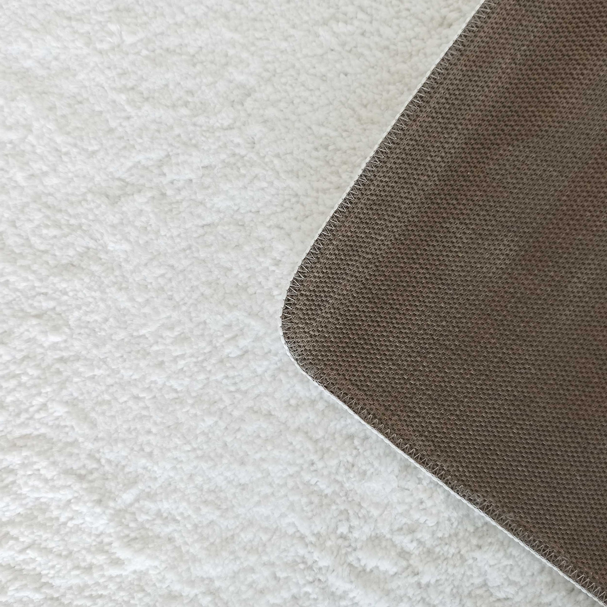 Gros plan sur un tapis blanc à la texture douce et moelleuse, montrant son dos tissé marron et la bordure cousue