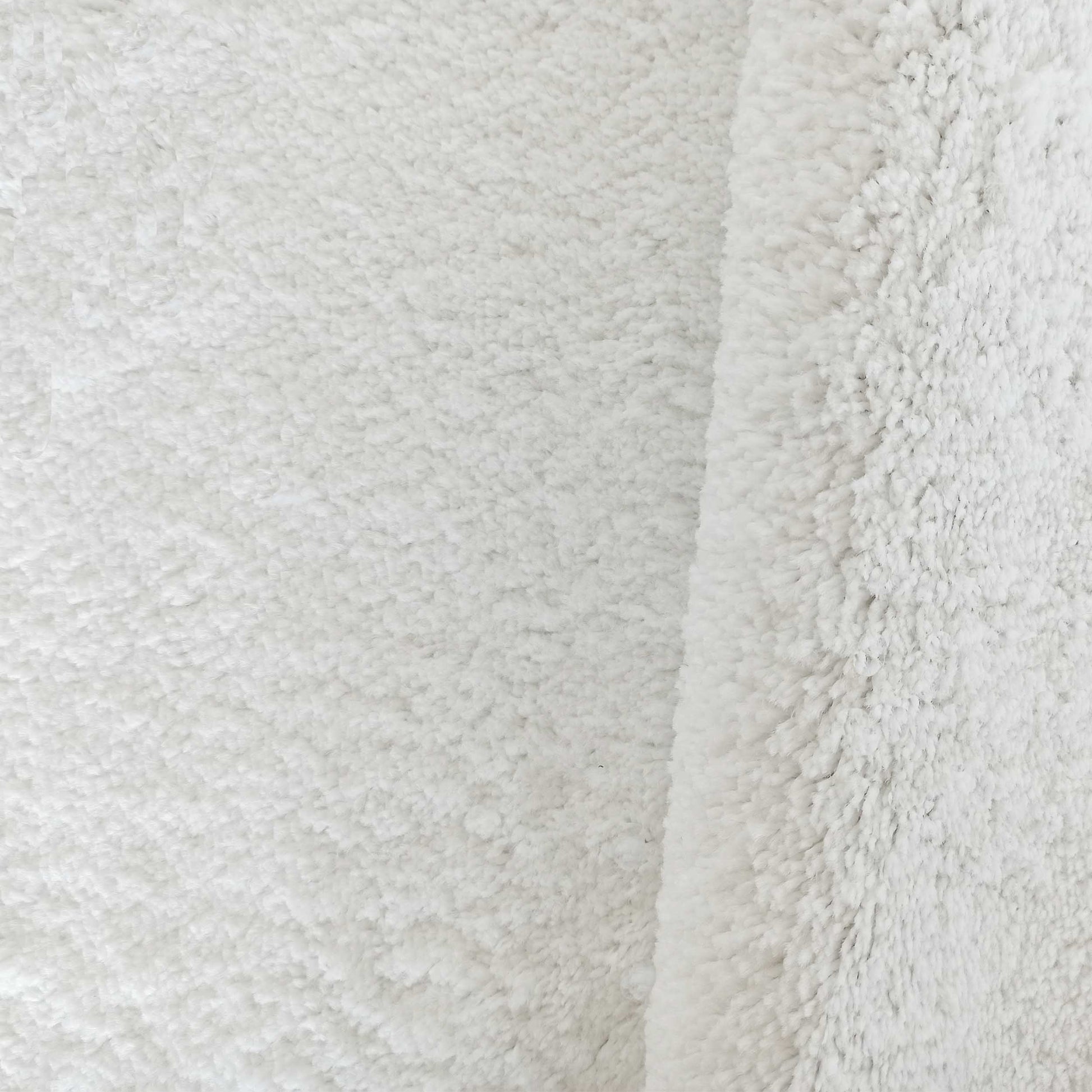 Tapis blanc doux et épais à poils longs, avec un léger pli sur le côté droit, montrant sa texture pelucheuse