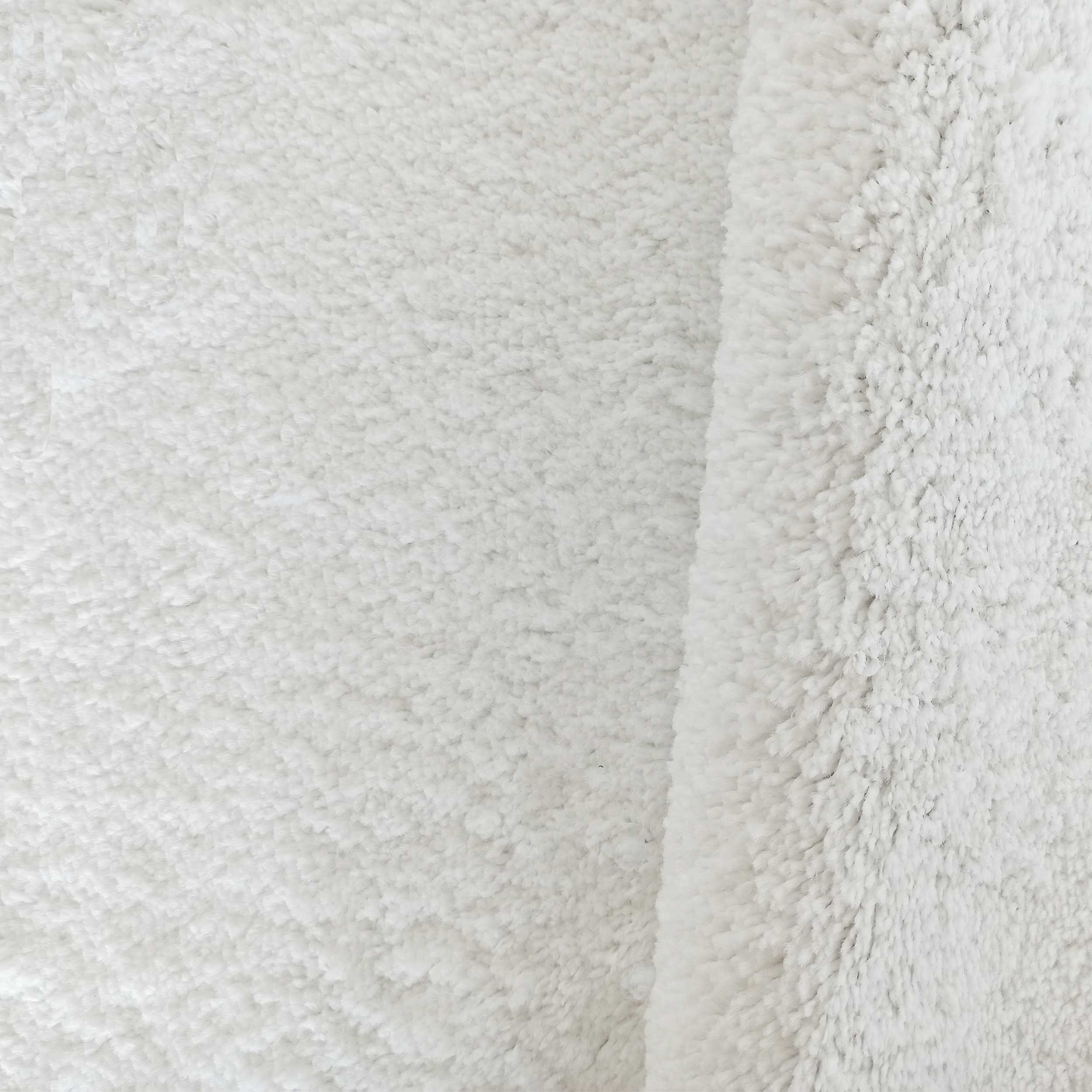 Tapis blanc doux et épais à poils longs, avec un léger pli sur le côté droit, montrant sa texture pelucheuse