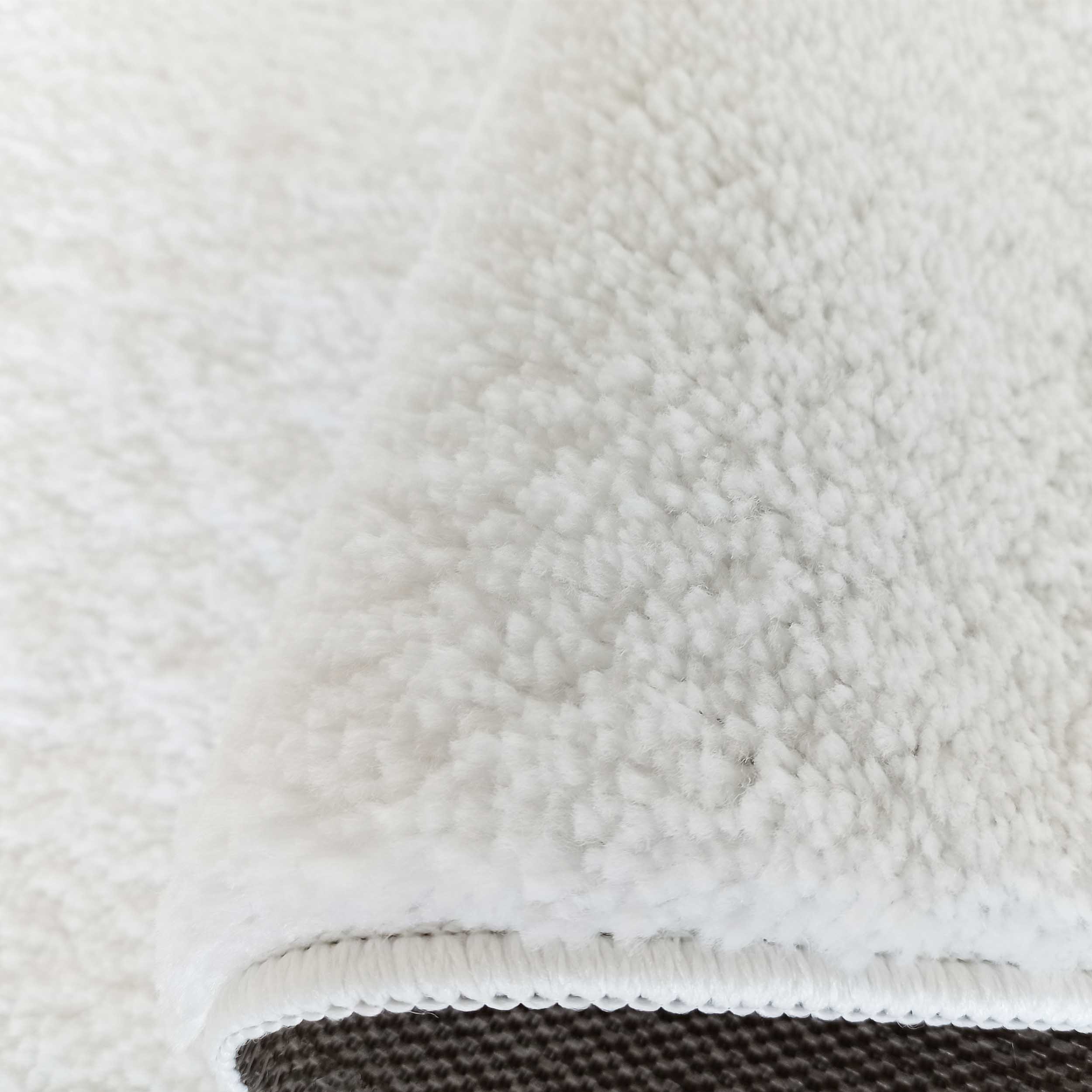 Gros plan d'un tapis blanc à poils longs et texture moelleuse, son bord est visible ainsi que son envers foncé et texturé