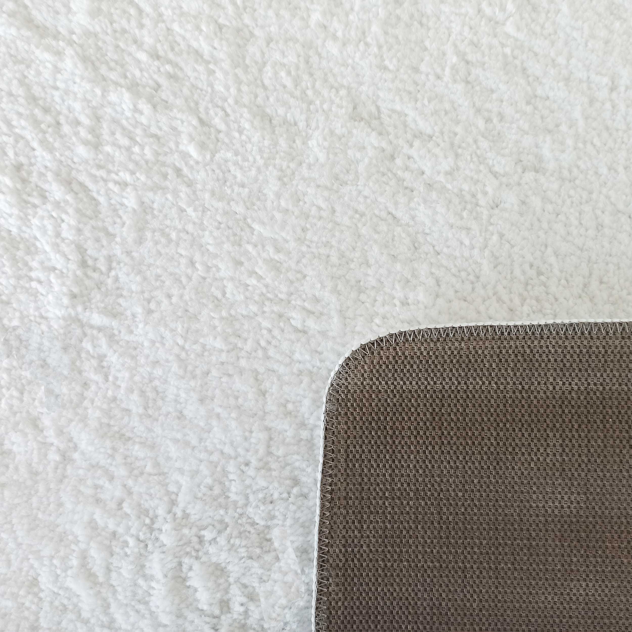 Tapis blanc moelleux à poils longs avec une bordure cousue et un envers antidérapant marron texturé