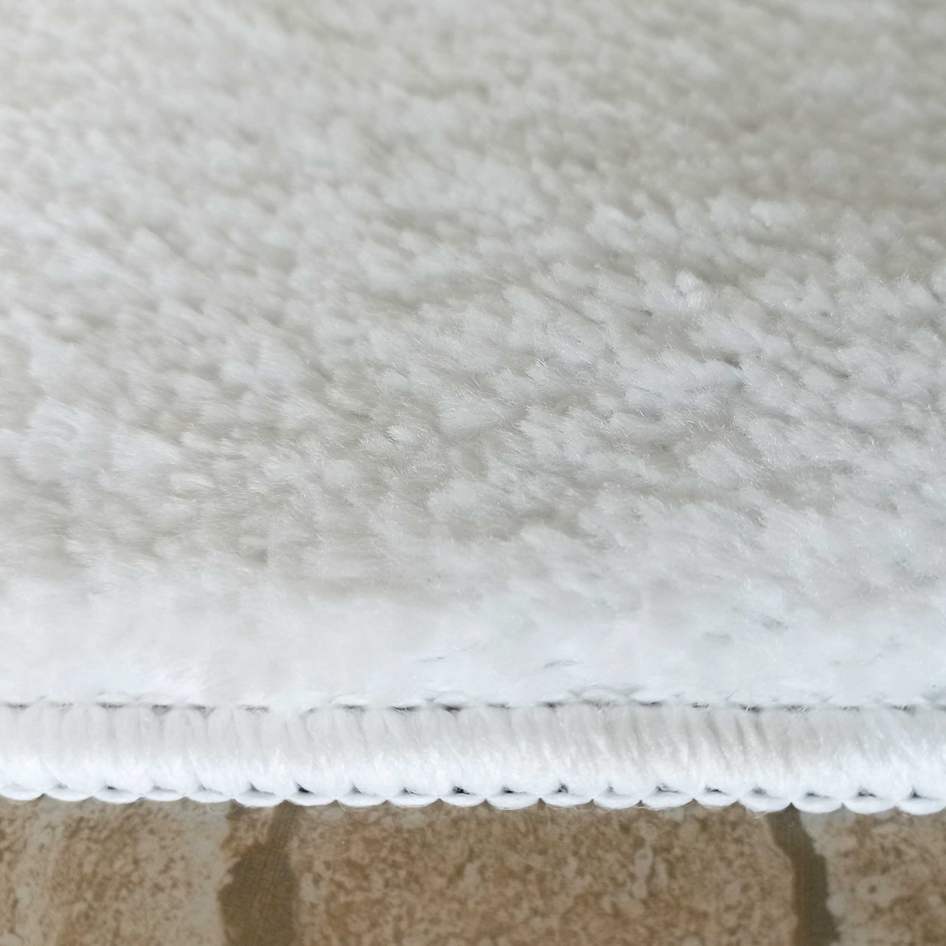 Tapis blanc doux et duveteux à poils longs, avec un bord surpiqué, posé sur un sol carrelé marron clair