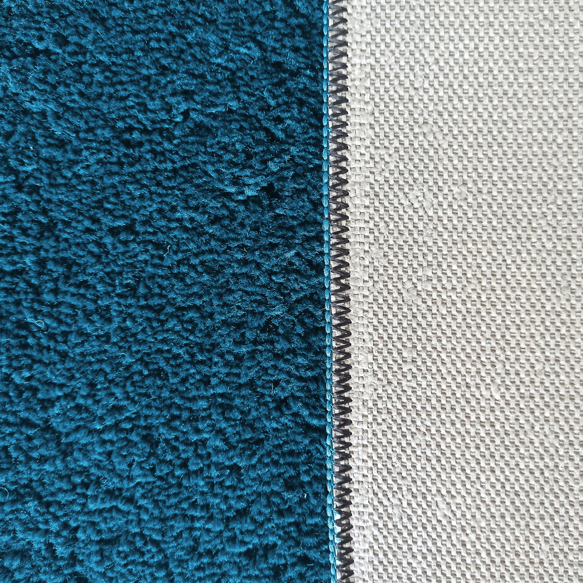 Gros plan sur un tapis présentant un côté turquoise à fibres épaisses et son dos en toile tissée gris clair, avec une couture zigzag