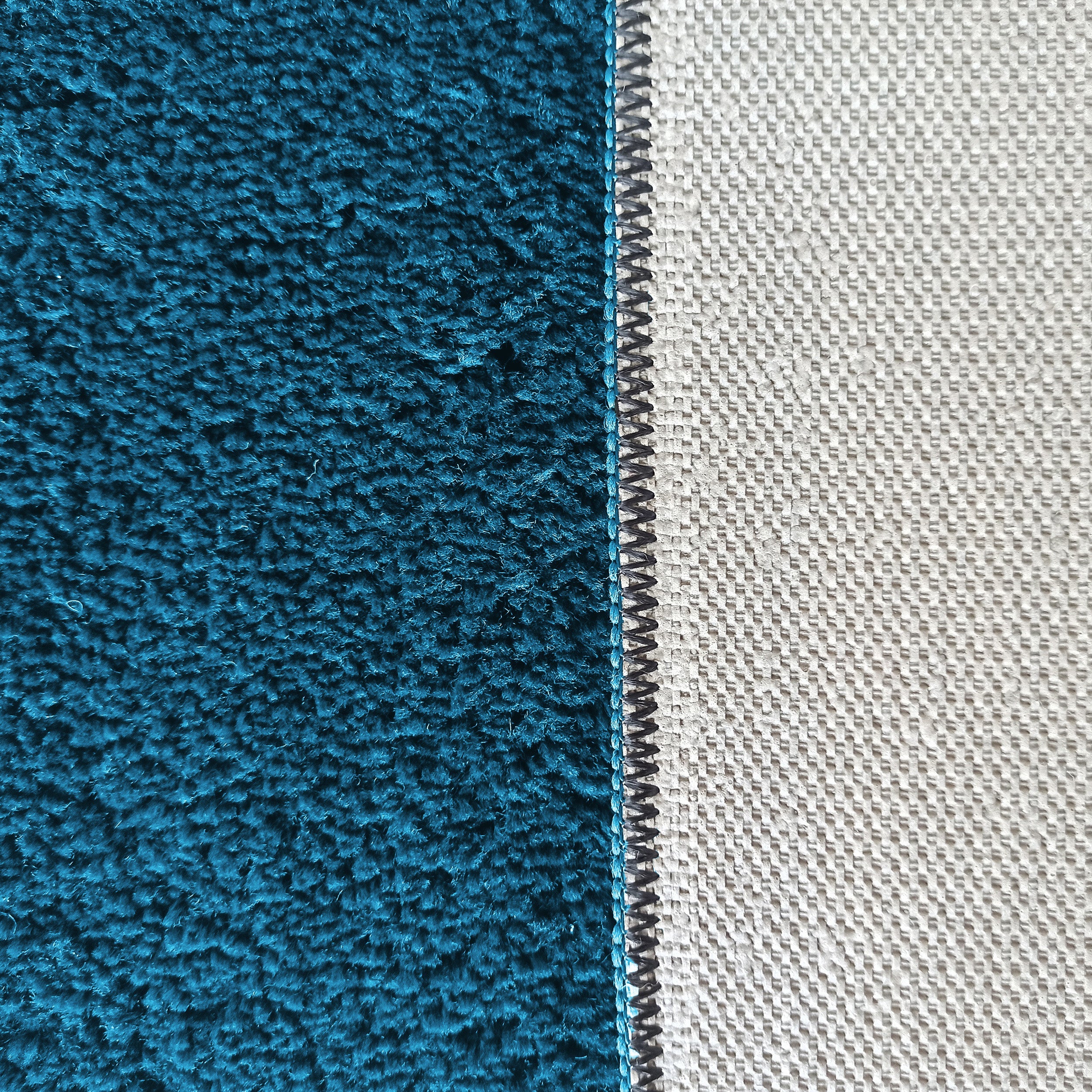 Gros plan sur un tapis présentant un côté turquoise à fibres épaisses et son dos en toile tissée gris clair, avec une couture zigzag