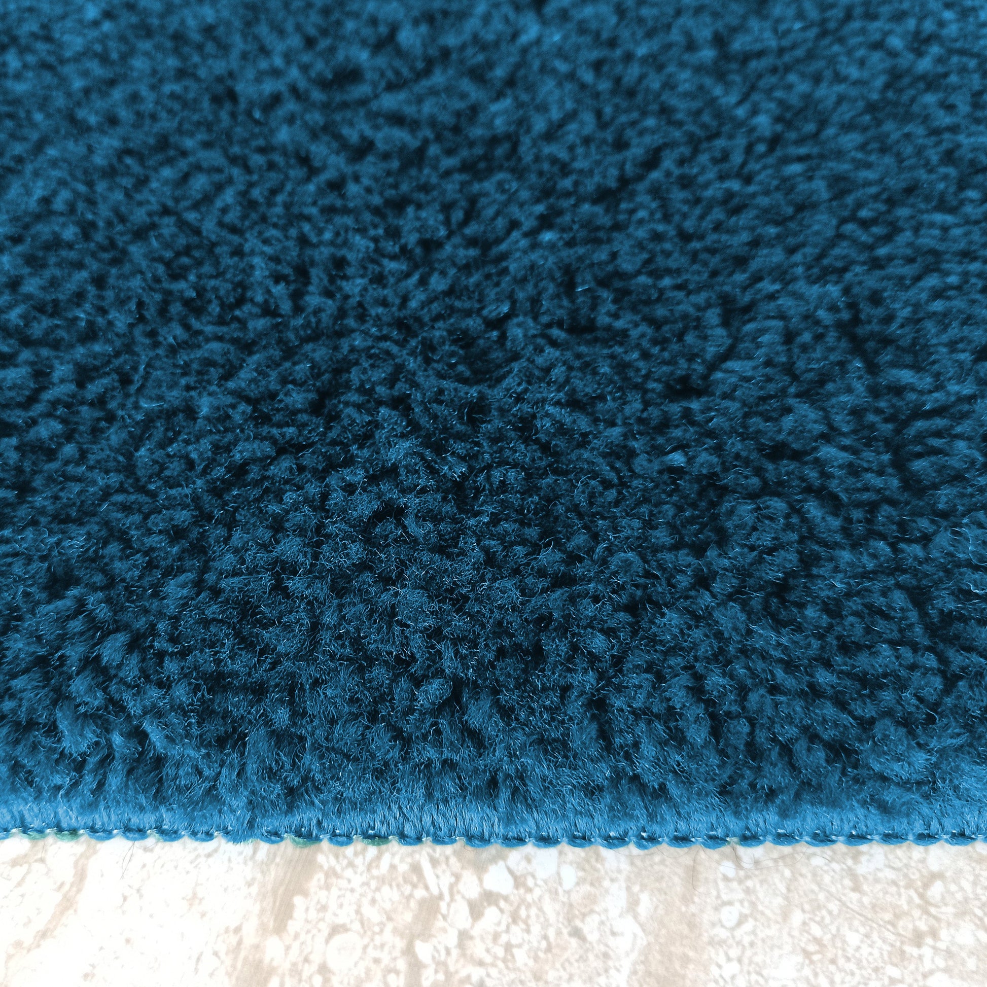 Gros plan sur un tapis moelleux bleu pétrole aux poils longs et à la texture dense, posé sur un sol clair