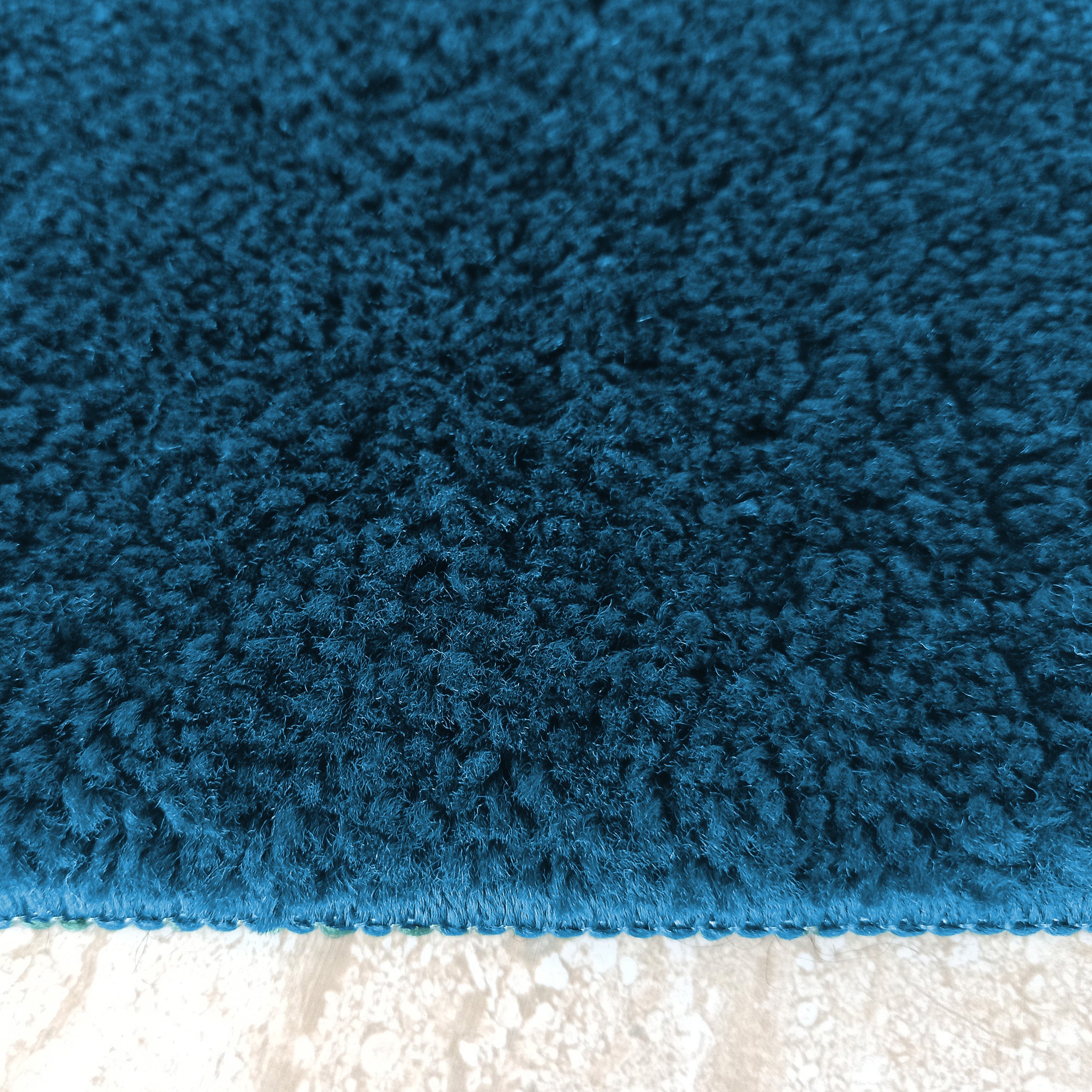 Gros plan sur un tapis moelleux bleu pétrole aux poils longs et à la texture dense, posé sur un sol clair
