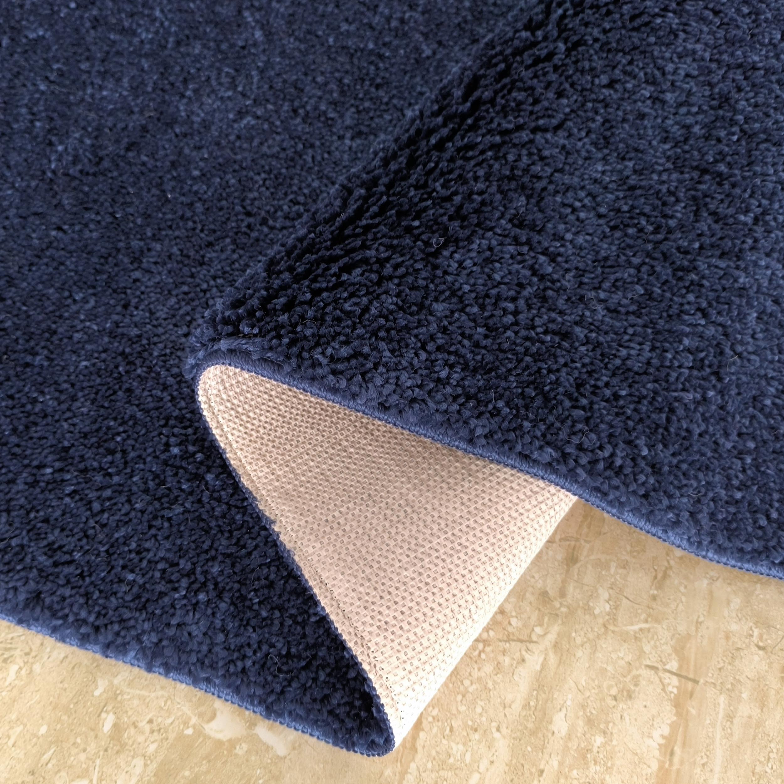 Tapis bleu marine avec une texture bouclée moelleuse, partiellement plié pour montrer l'envers beige antidérapant sur un sol clair