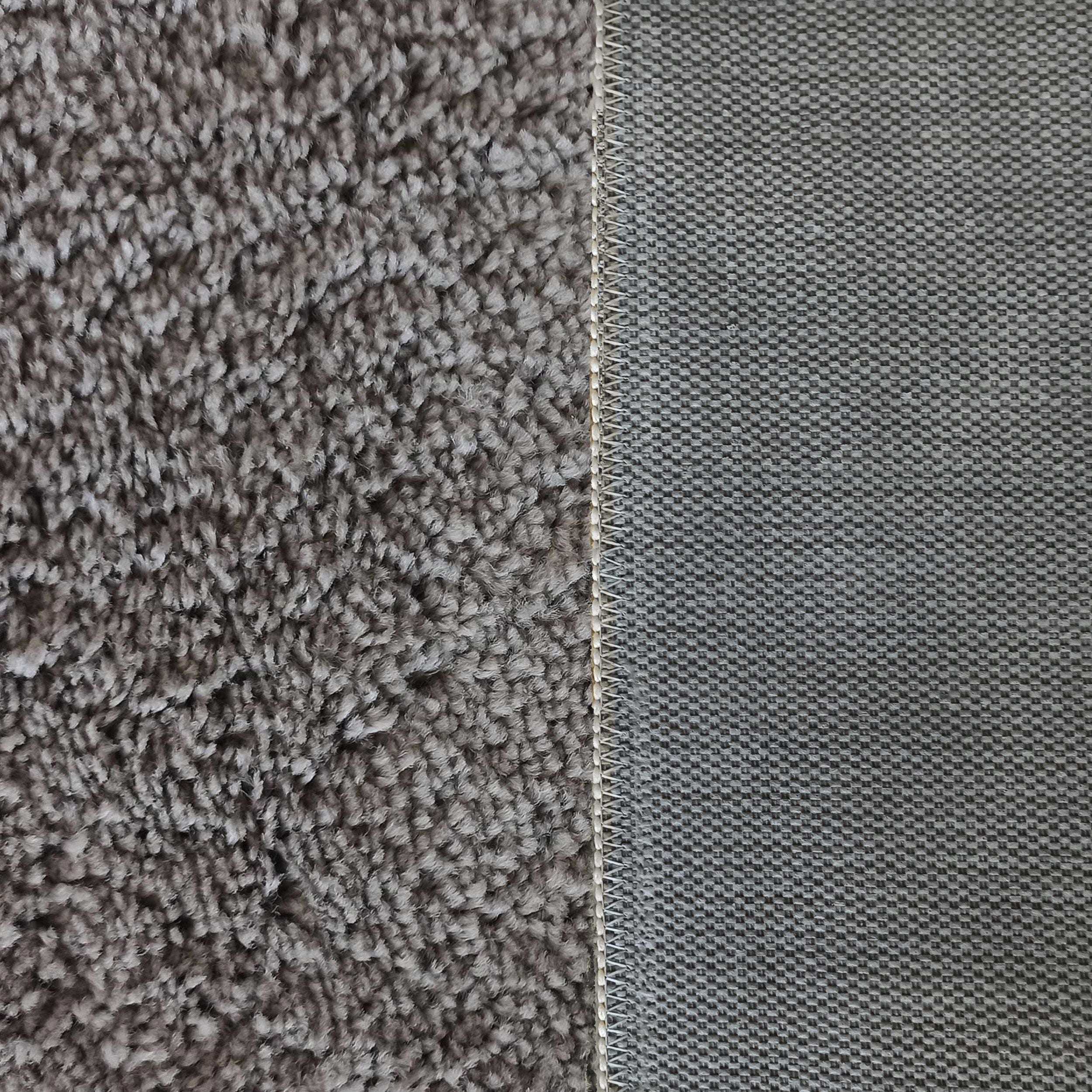 Tapis présentant sa face supérieure duveteuse gris-brun et son envers gris au tissage quadrillé, séparés par une couture beige