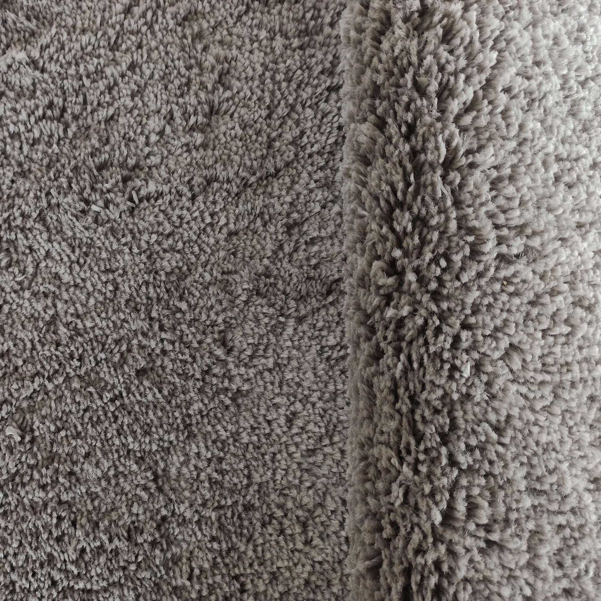 Gros plan sur un tapis texturé gris-taupe à poil long et doux, avec un bord légèrement replié sur la droite