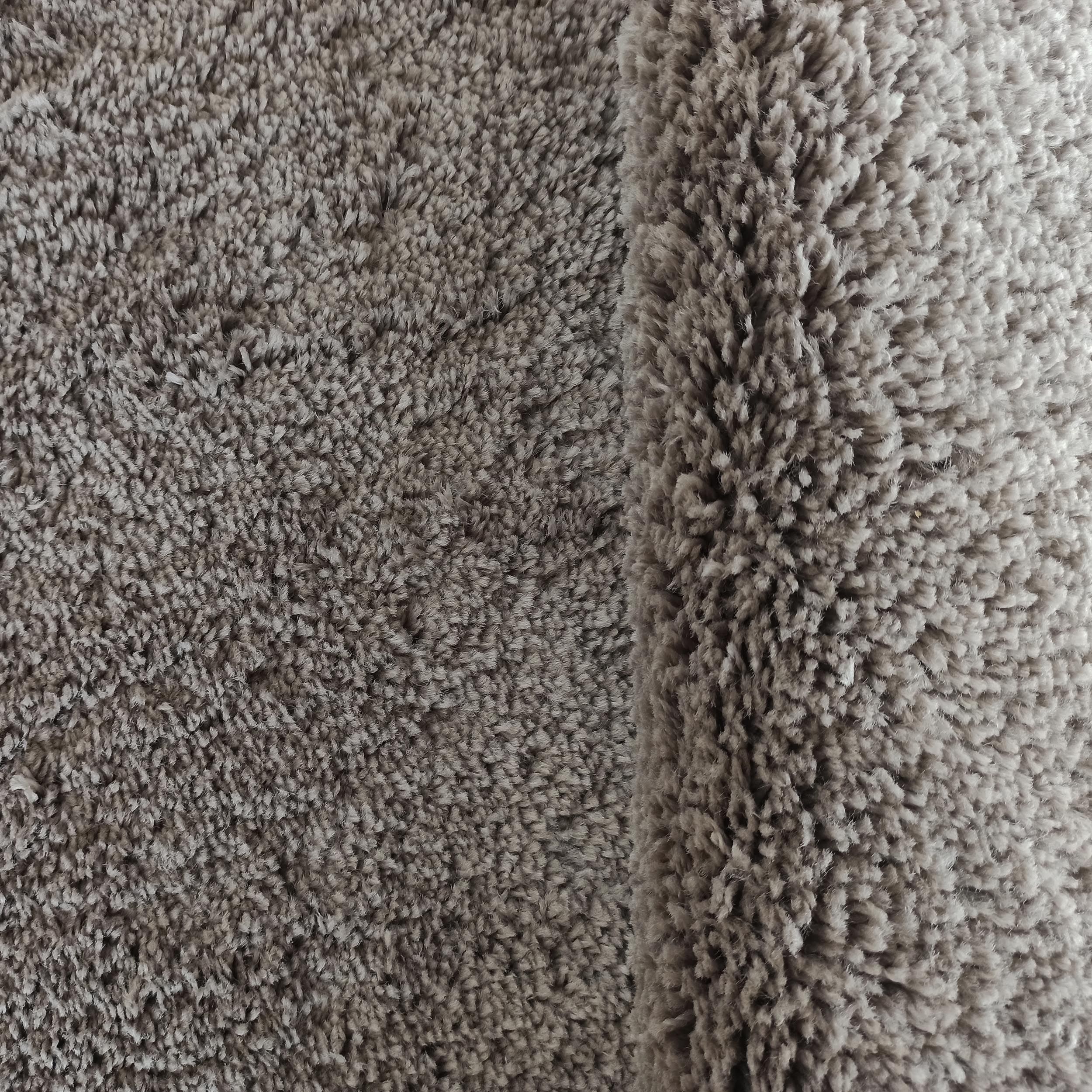 Gros plan sur un tapis texturé gris-taupe à poil long et doux, avec un bord légèrement replié sur la droite