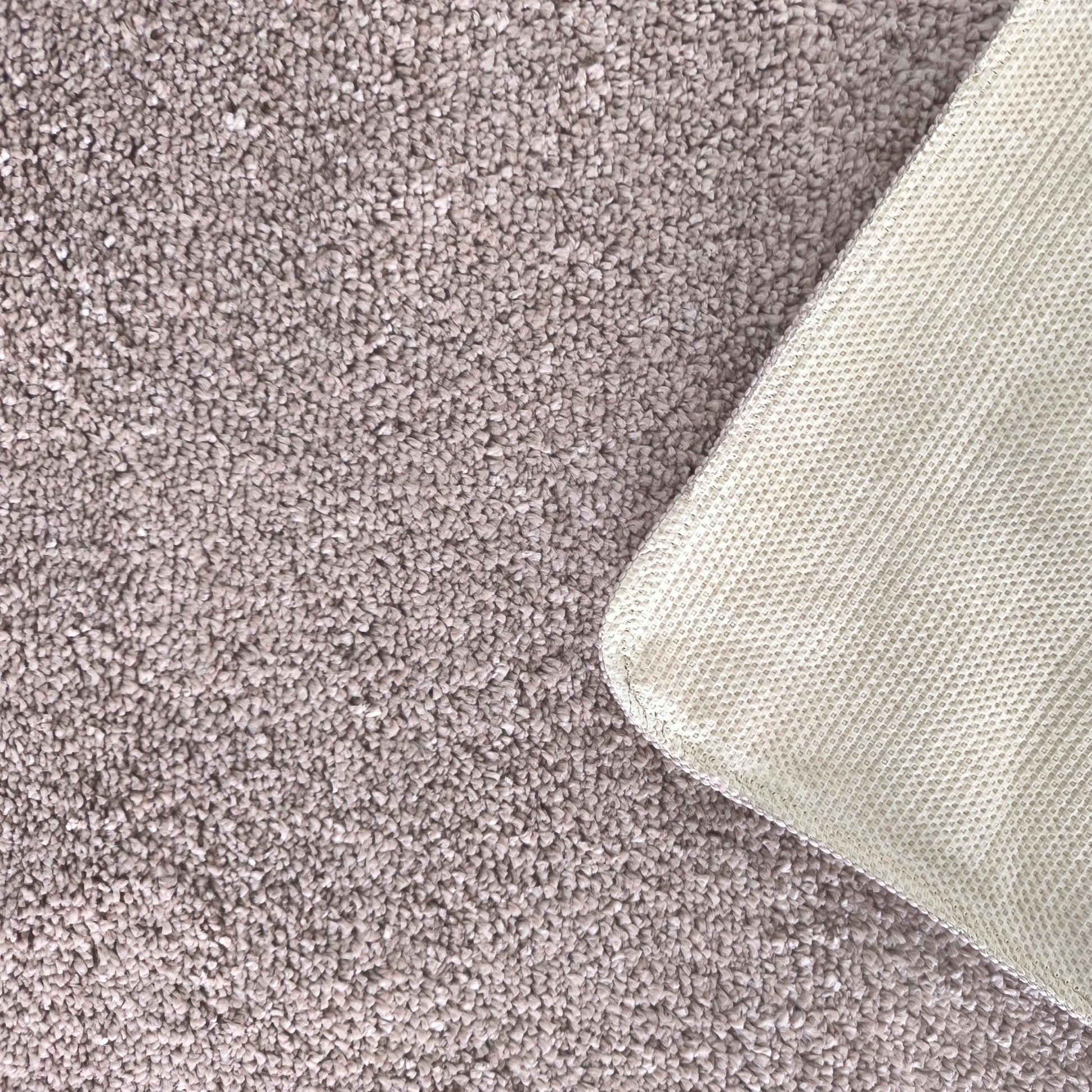 Tapis moelleux gris-brun avec une texture bouclée, le coin est relevé montrant le dessous quadrillé crème