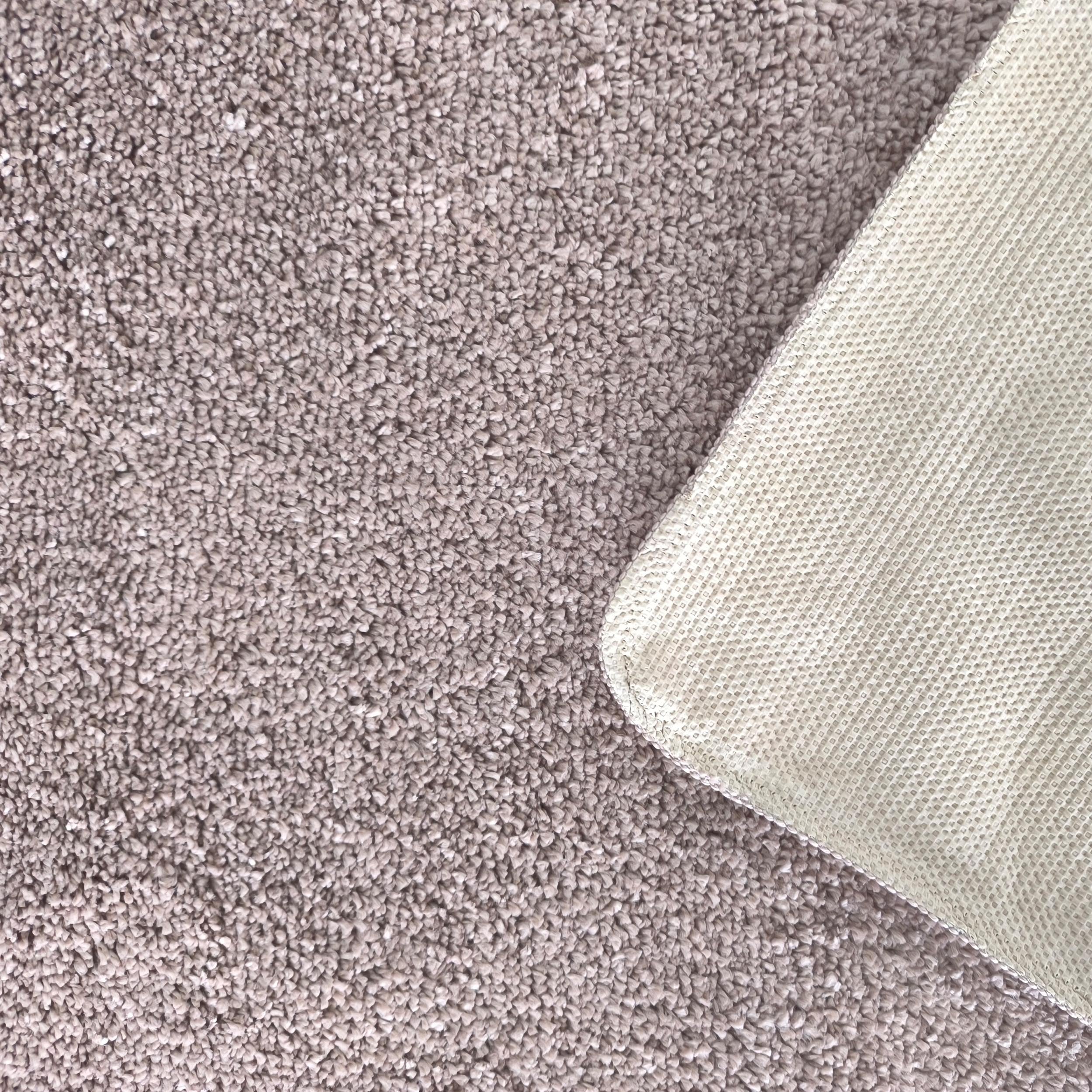 Tapis moelleux gris-brun avec une texture bouclée, le coin est relevé montrant le dessous quadrillé crème