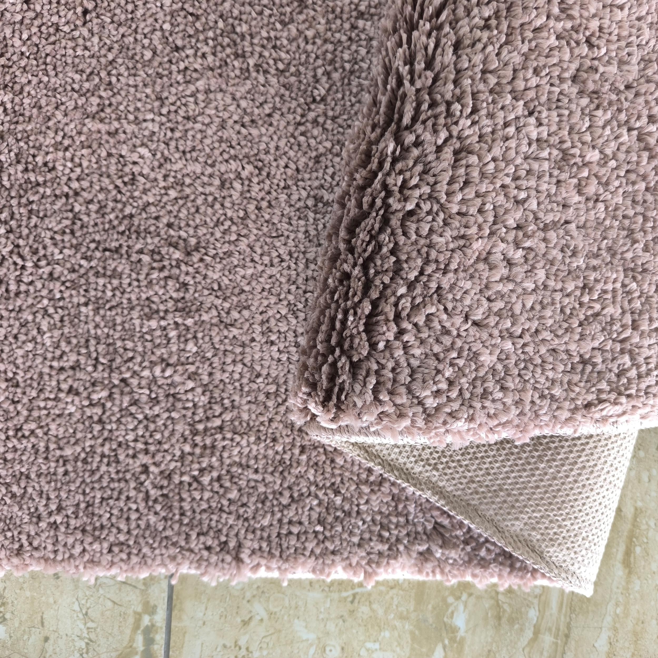 Tapis rose poudré à poils longs partiellement roulé, dévoilant son envers tissé et un sol carrelé beige clair