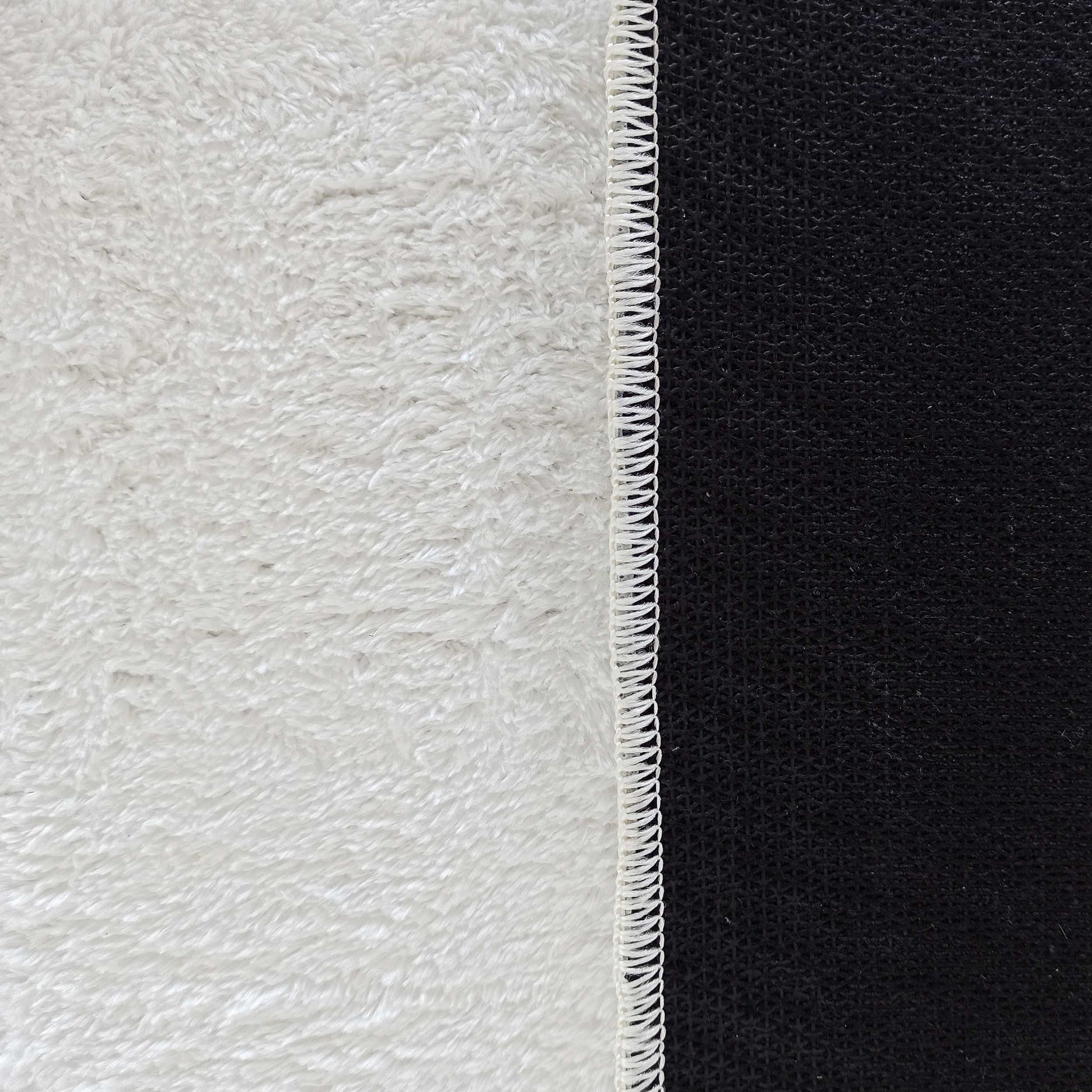 Tapis blanc à la texture dense et moelleuse, bordure blanche cousue et envers noir texturé quadrillé