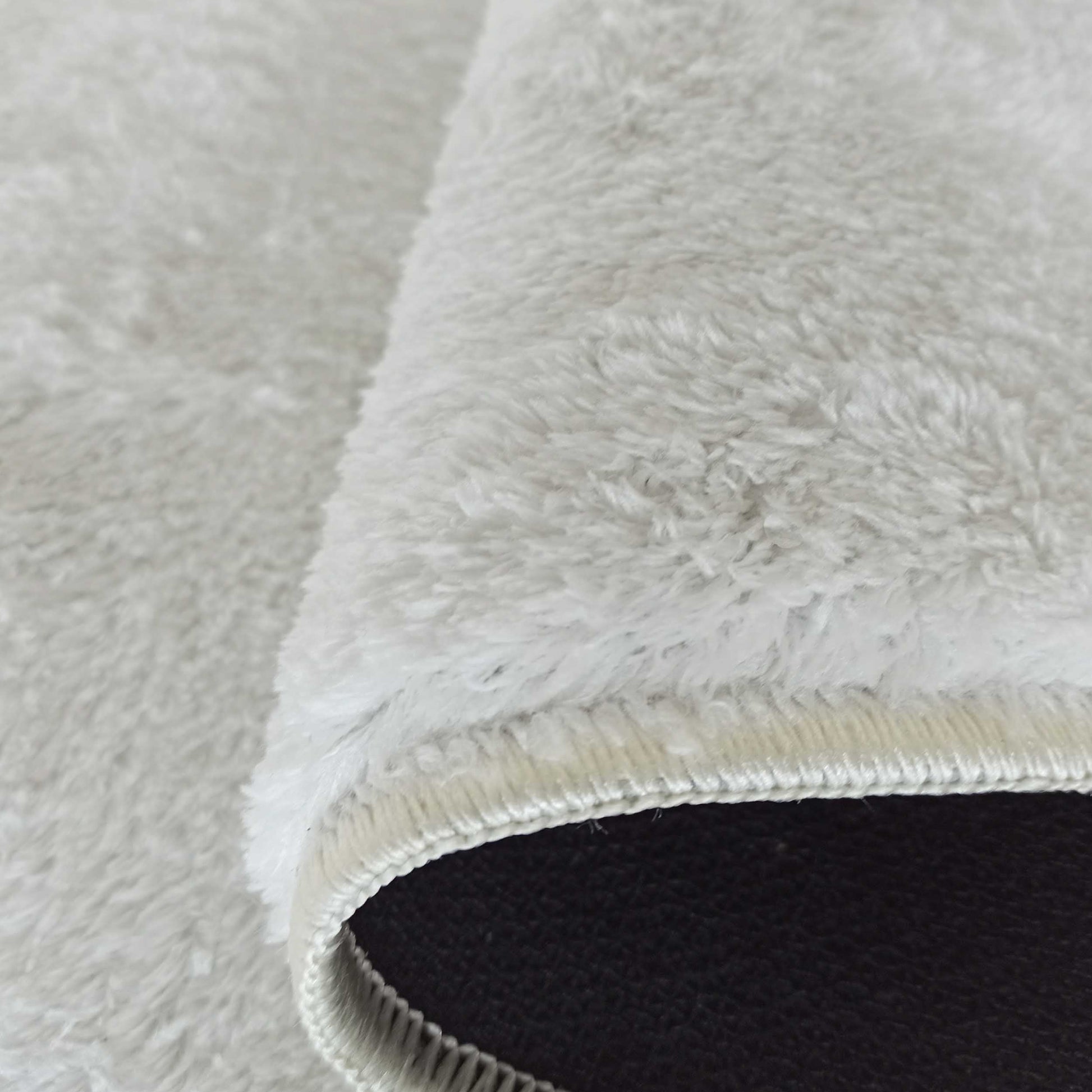 Tapis à longs poils gris très clair, enroulé sur lui-même, montrant sa semelle noire et sa bordure crème