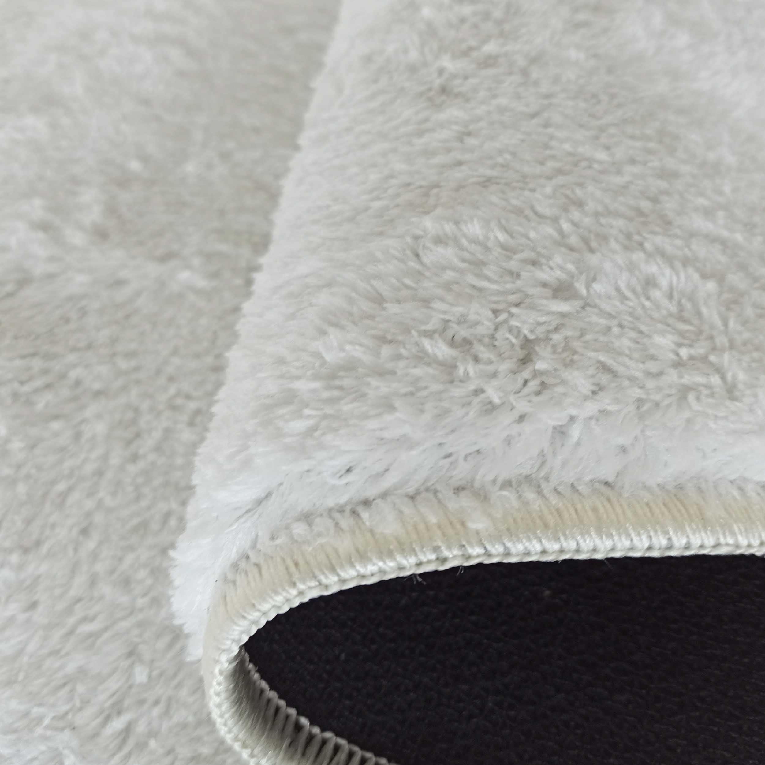 Tapis à longs poils gris très clair, enroulé sur lui-même, montrant sa semelle noire et sa bordure crème