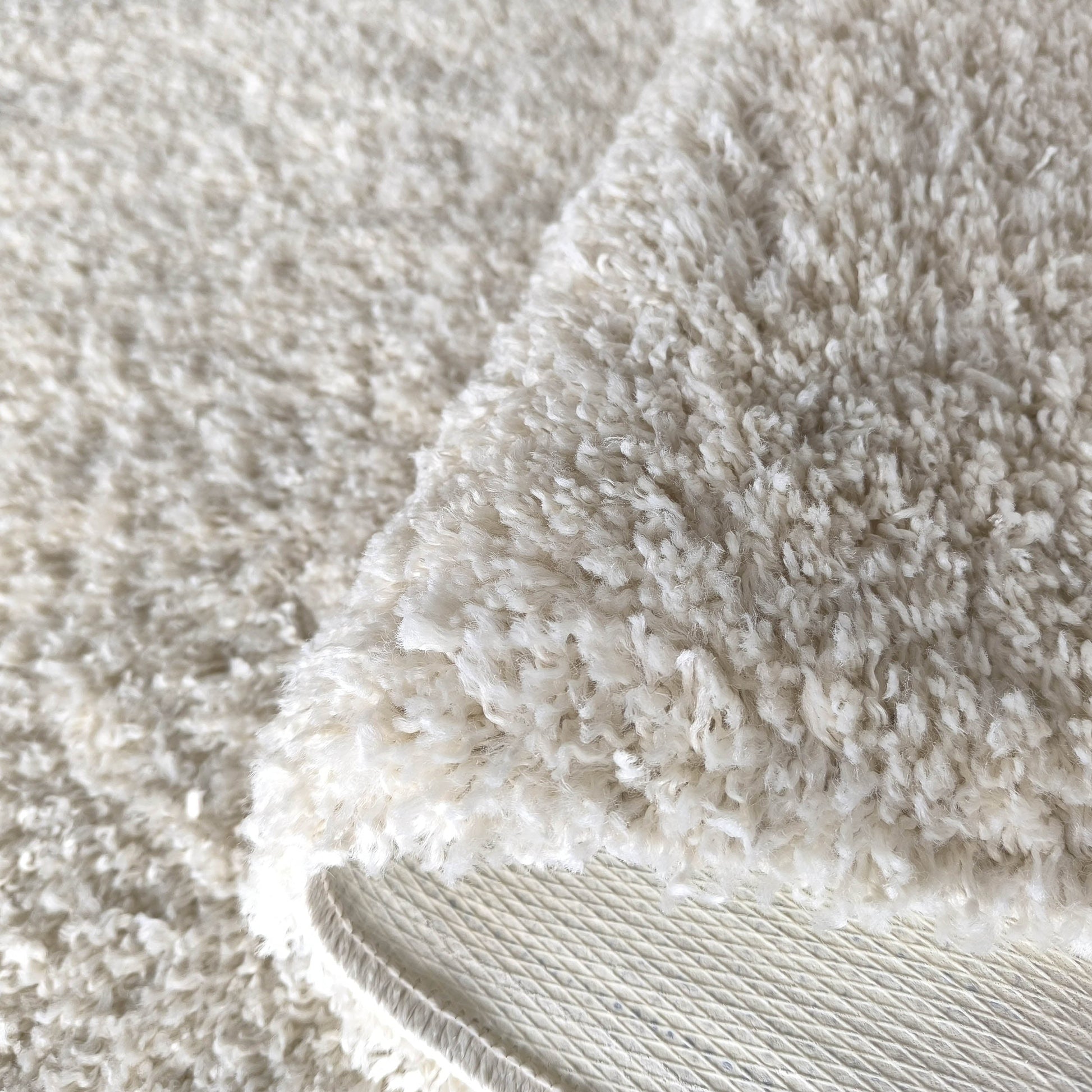 Tapis crème à texture shaggy, replié pour révéler son envers blanc cassé texturé de losanges