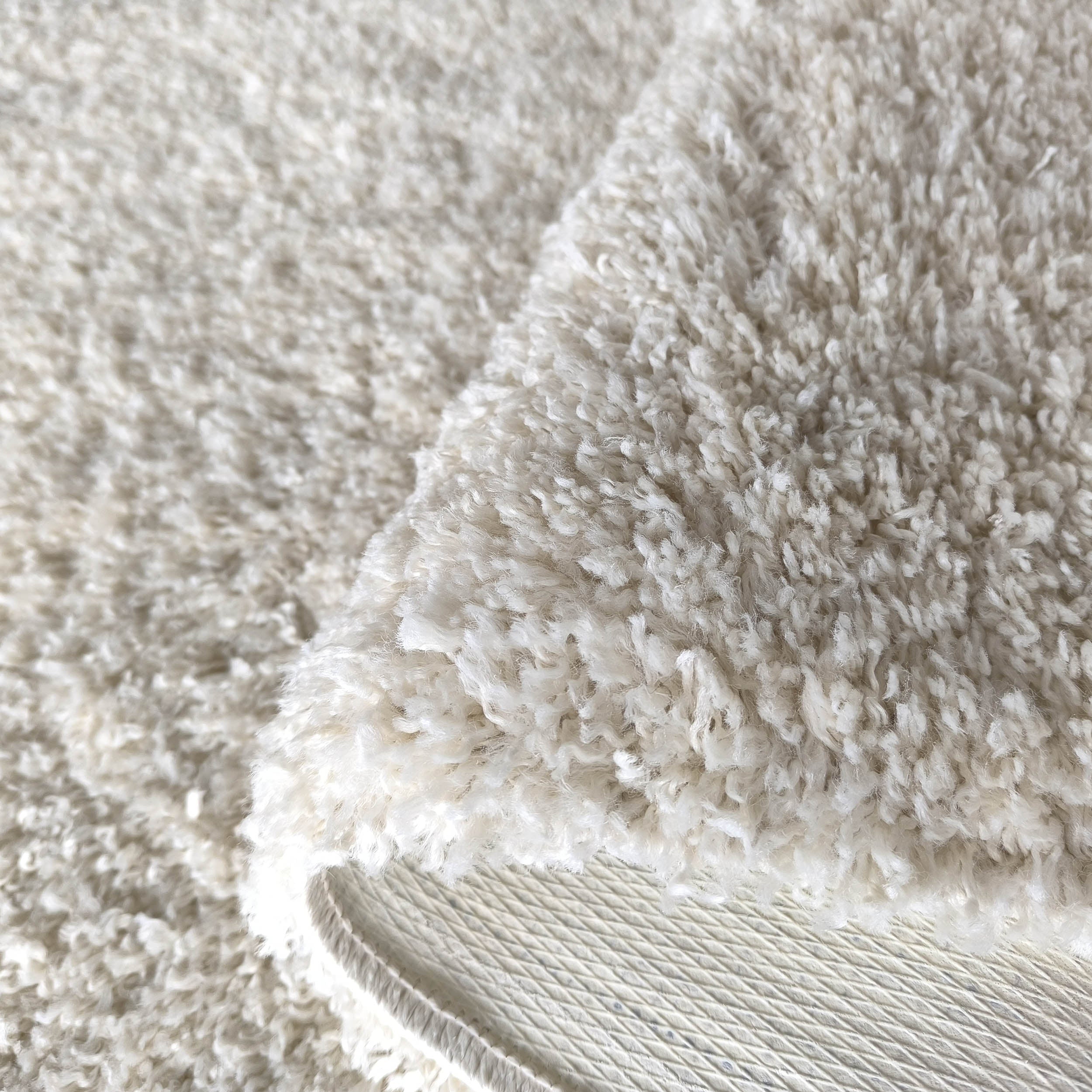 Tapis crème à texture shaggy, replié pour révéler son envers blanc cassé texturé de losanges