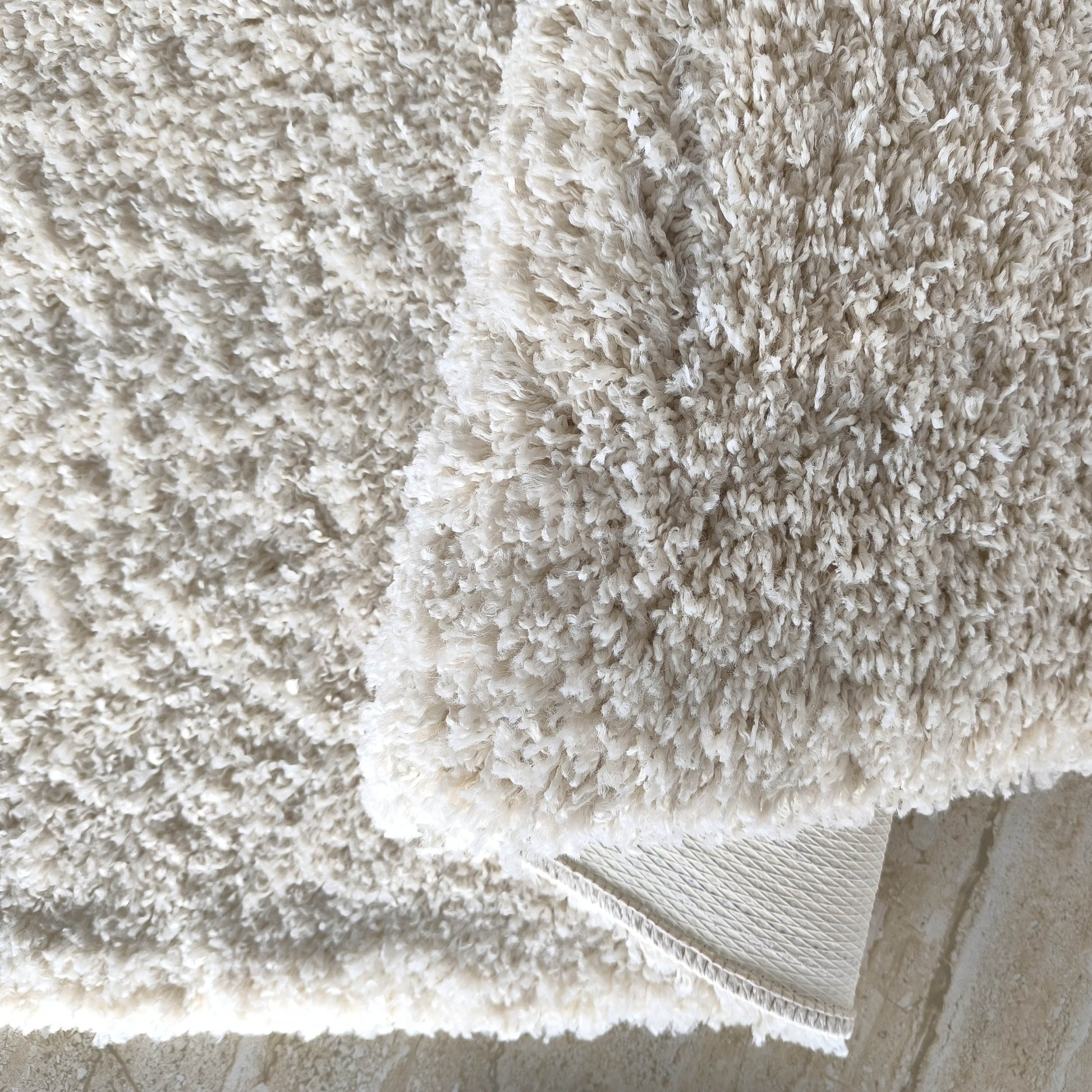 Tapis moelleux et blanc cassé à longs poils bouclés, partiellement replié, laissant apparaître son envers sur un sol beige