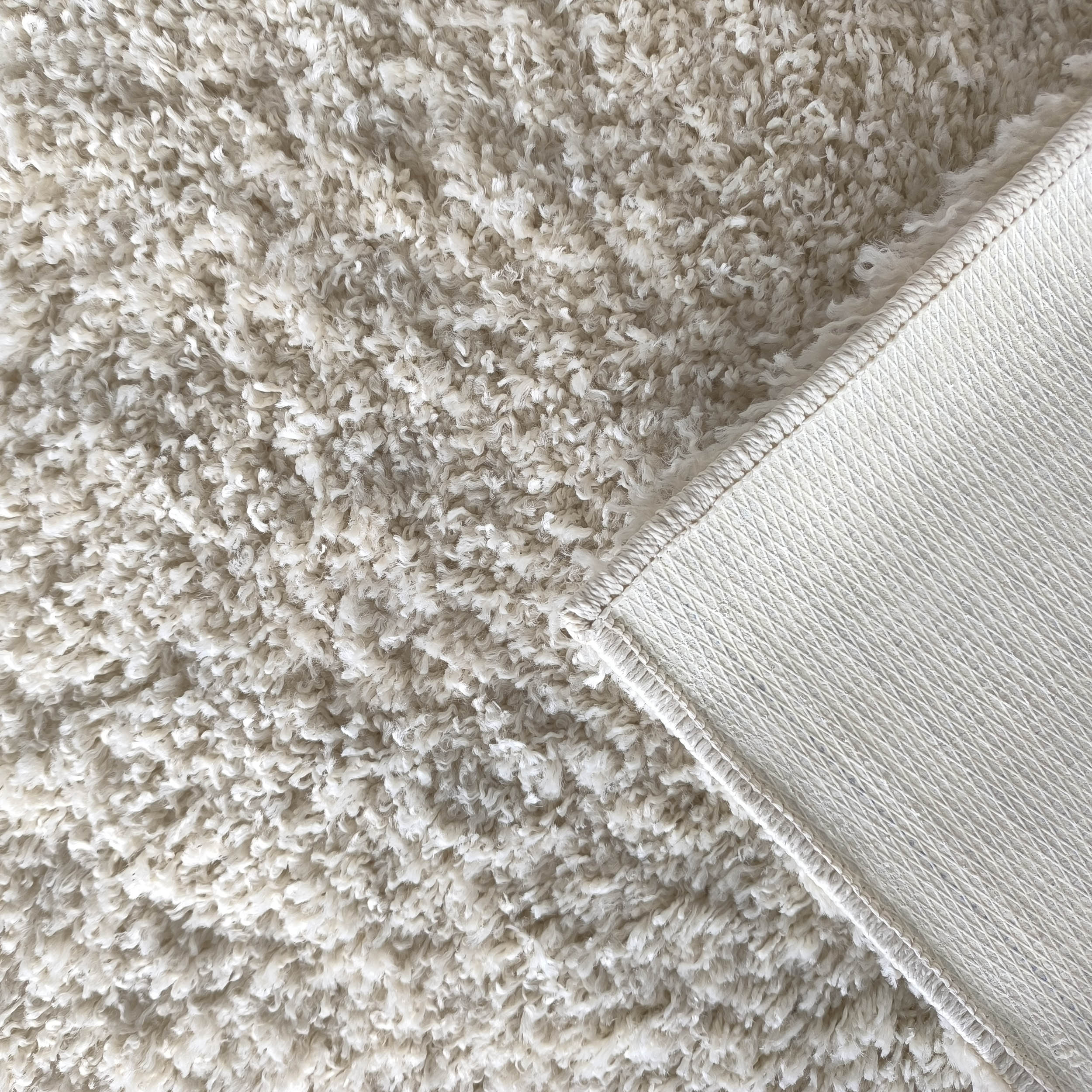 Tapis en boucles serrées de couleur écru ou blanc cassé, avec un coin relevé montrant son envers texturé antidérapant