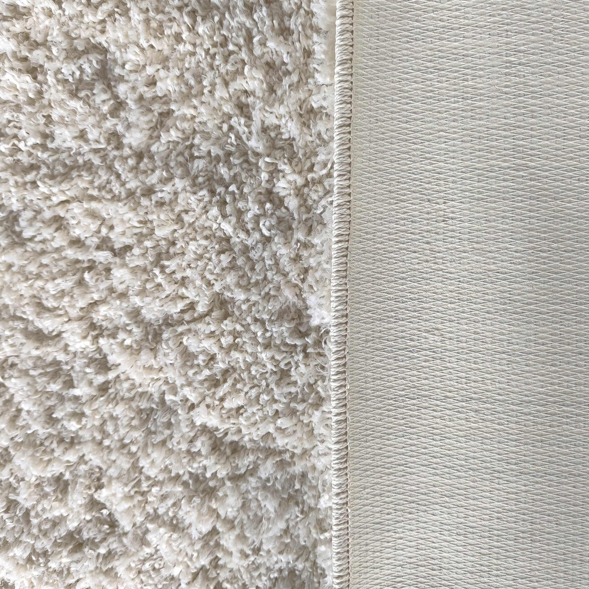 Tapis crème à la texture douce et bouclée, avec une bordure visible et un envers gris clair à motif losanges