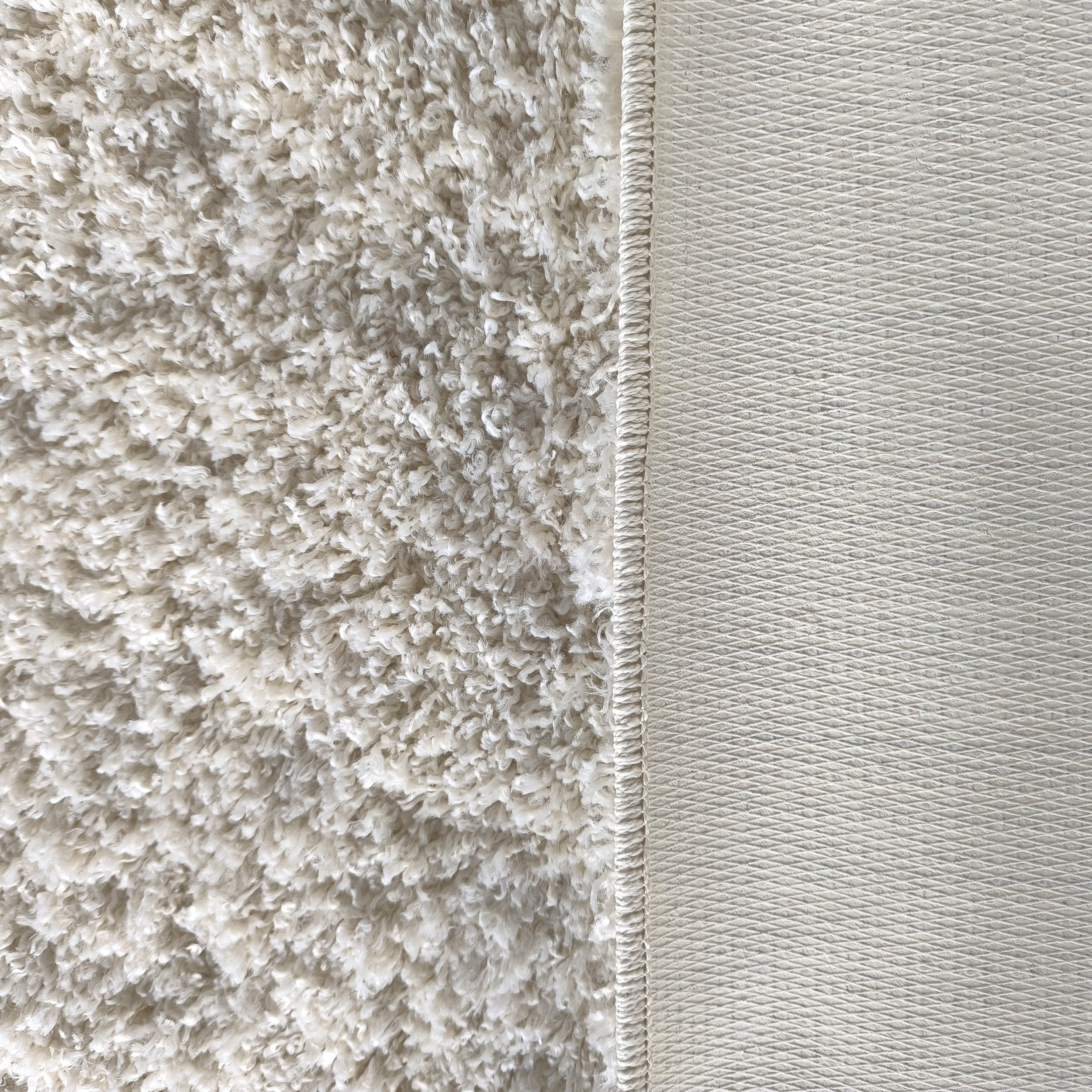 Tapis crème à la texture douce et bouclée, avec une bordure visible et un envers gris clair à motif losanges